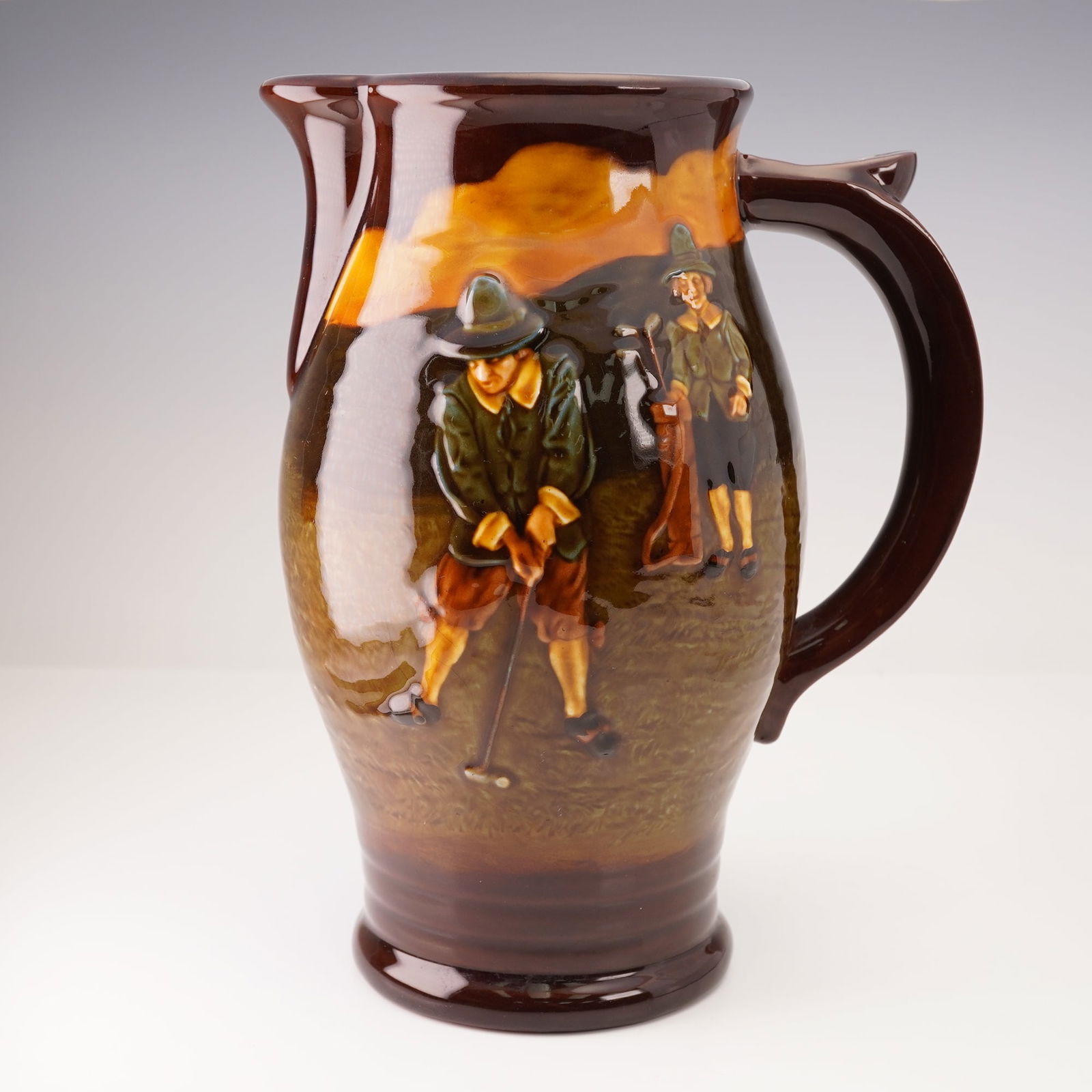 Royal Doulton Large Sized Kingsware Jug, Golfers: This Royal Doulton Kingsware Golfer's Jug features beautifully detailed relief molded golfers in action, set against a rich brown glaze. The images of the golfers, dressed in traditional golfing attir
