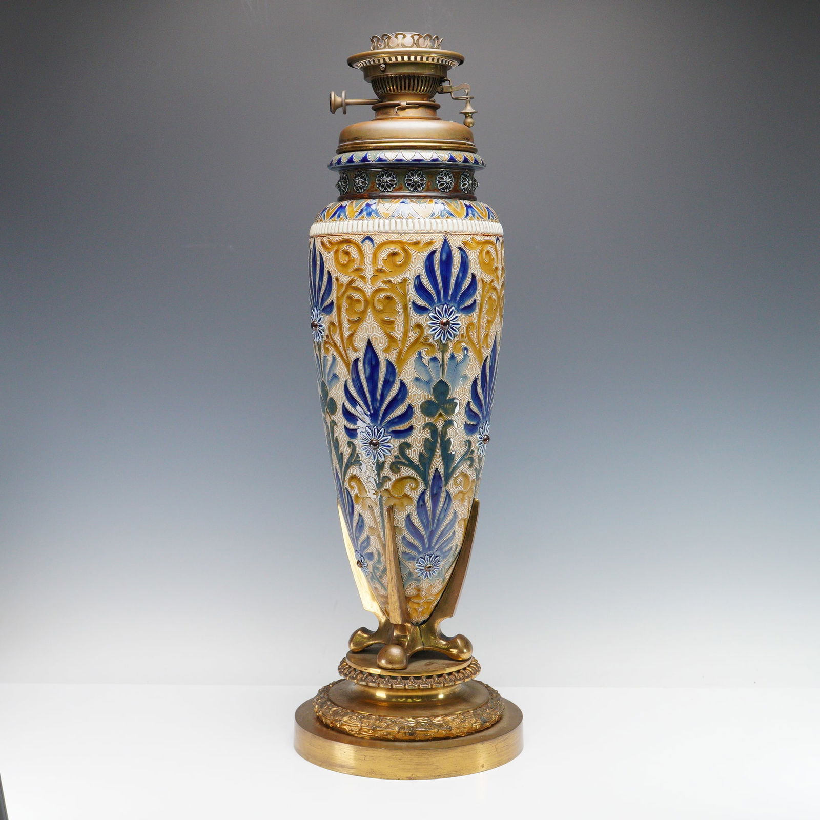 Doulton Lambeth by Edith Lupton Stoneware Oil Lamp: Impressive and large, stoneware oil lamp within a polished brass base, by Hinks and Sons London. This Victorian lamp of tapering baluster body richly decorated in relief with scrolling foliate panels