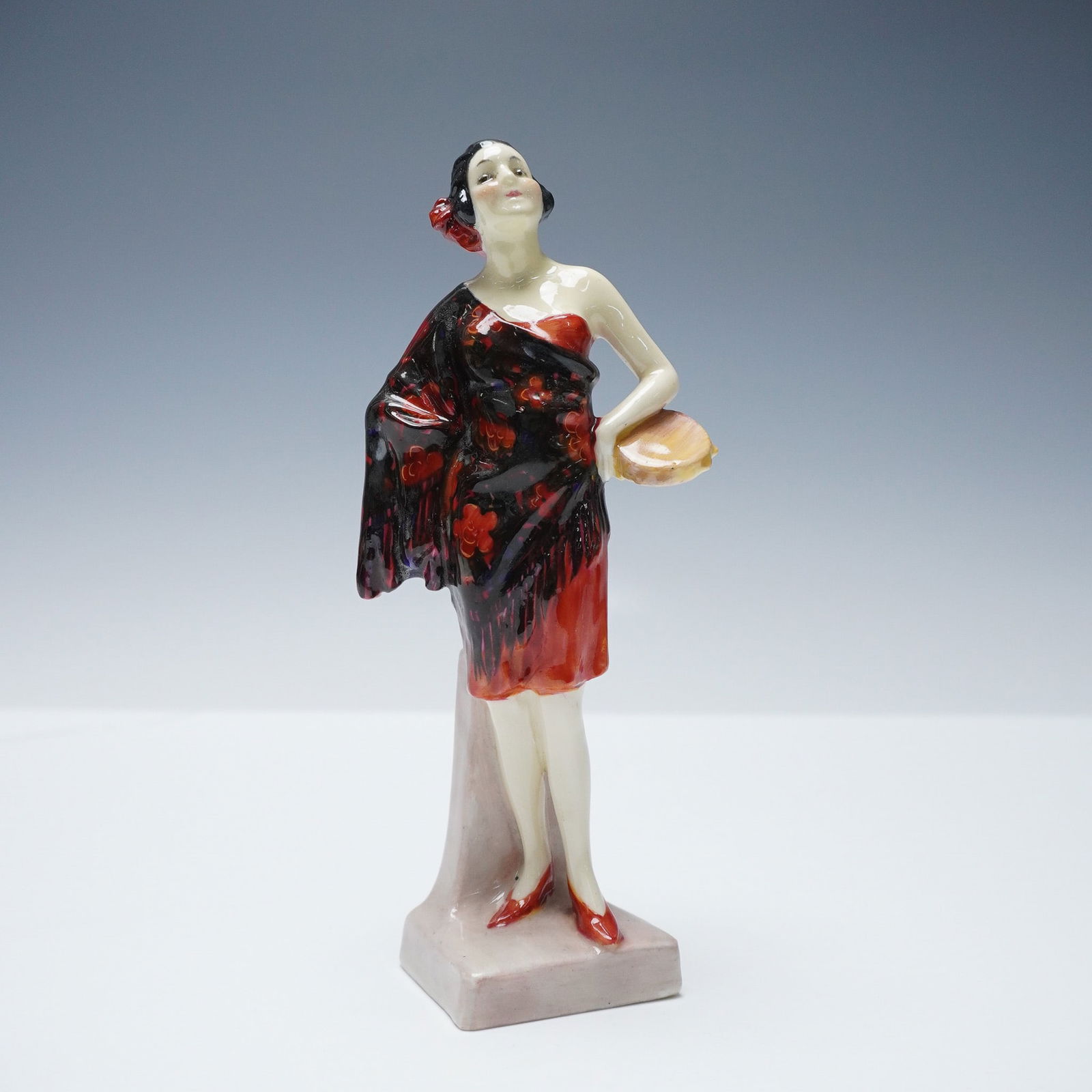 Royal Doulton Figurine, Carmen HN1267: This early 20th-century model features a standing woman wearing a red dress with a black floral shawl. The figure is depicted with one hand on her hip and the other holding a tambourine, with a red