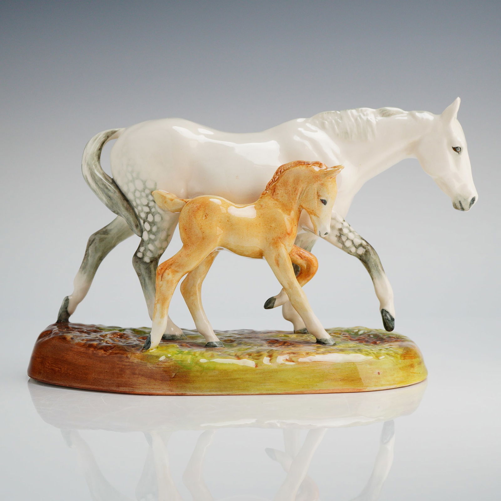 Royal Doulton The Gude Grey Mare and Foal Figurine HN 2532.G: A single glazed porcelain figurine group by Royal Doulton, titled "The Gude Grey Mare." The sculpture depicts a mare and her foal standing on an oval, naturalistic base finished in green, yellow, and