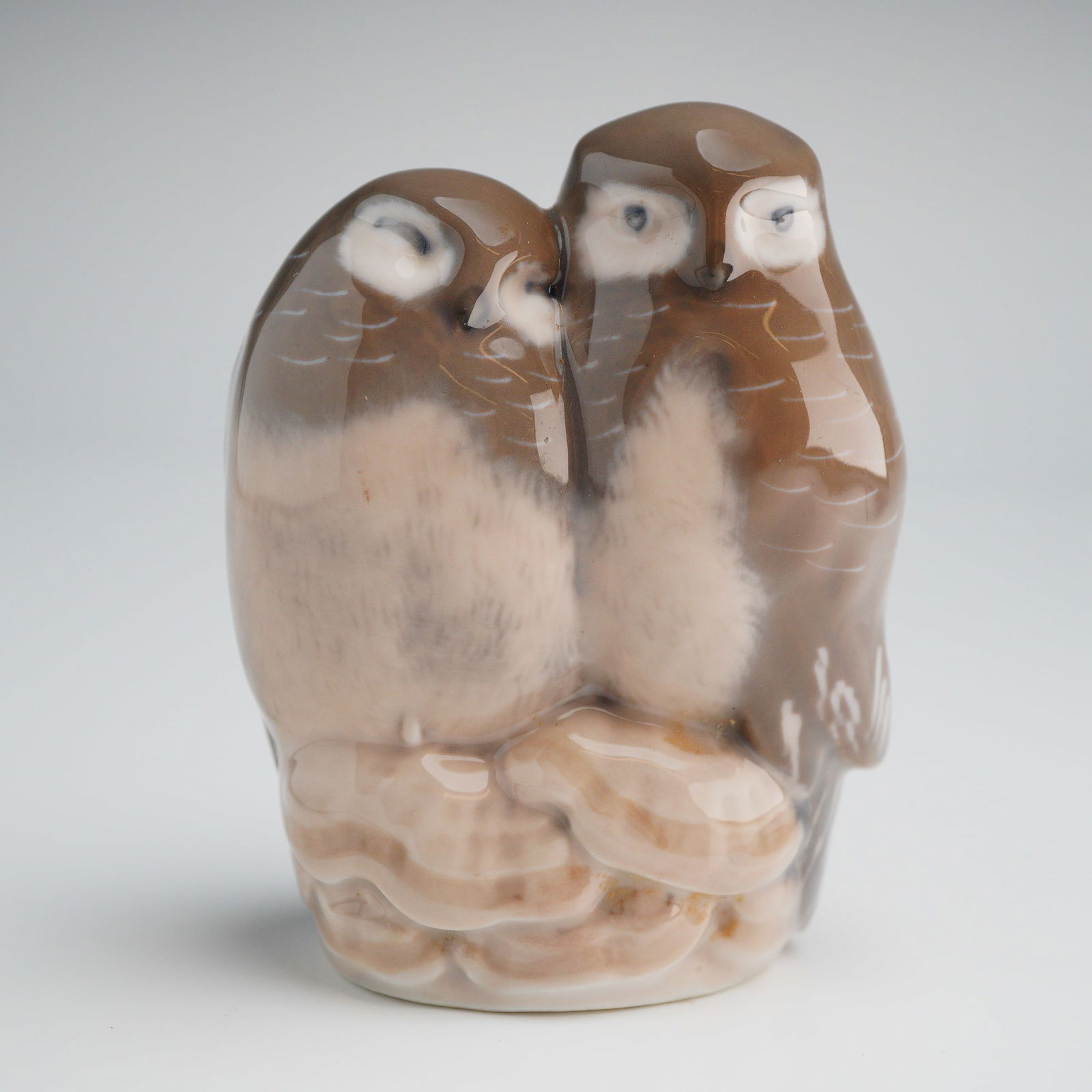 Royal Copenhagen Porcelain Figurine, Owls Model 834: A single glazed porcelain figurine by Royal Copenhagen, depicting a naturalistic representation of two snuggling owls resting on a textured base. The piece is executed in brown, beige, and white color