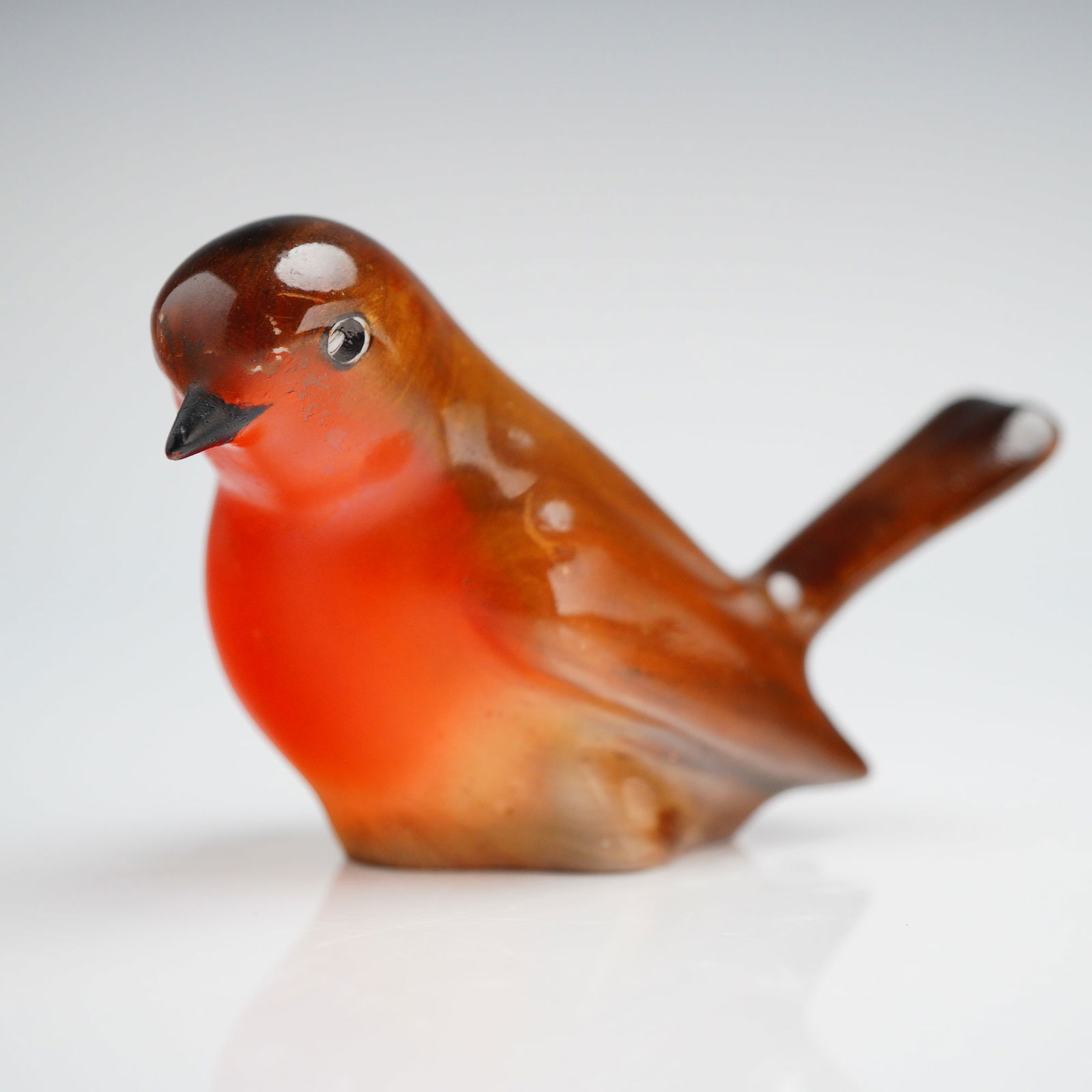 A Doulton Glazed Ceramic Robin Figurine: A single glazed ceramic figurine depicting a robin in a naturalistic pose. The item is finished with a high-gloss glaze, featuring reddish-brown tones on the back and wings, transitioning to a bright