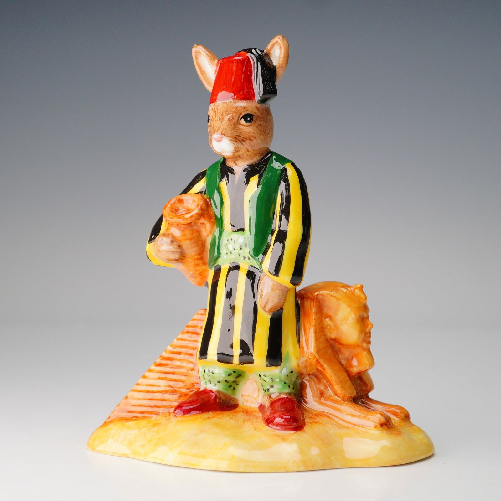 Royal Doulton Colorway Prototype Egyptian Bunnykins: Egyptian colorway bunnykins modeled wearing a black and yellow striped attire with red fez. The pyramid and Sphynx is painted in a golden sand hue. Prototype Only backstamp. Royal Doulton backstamp. 