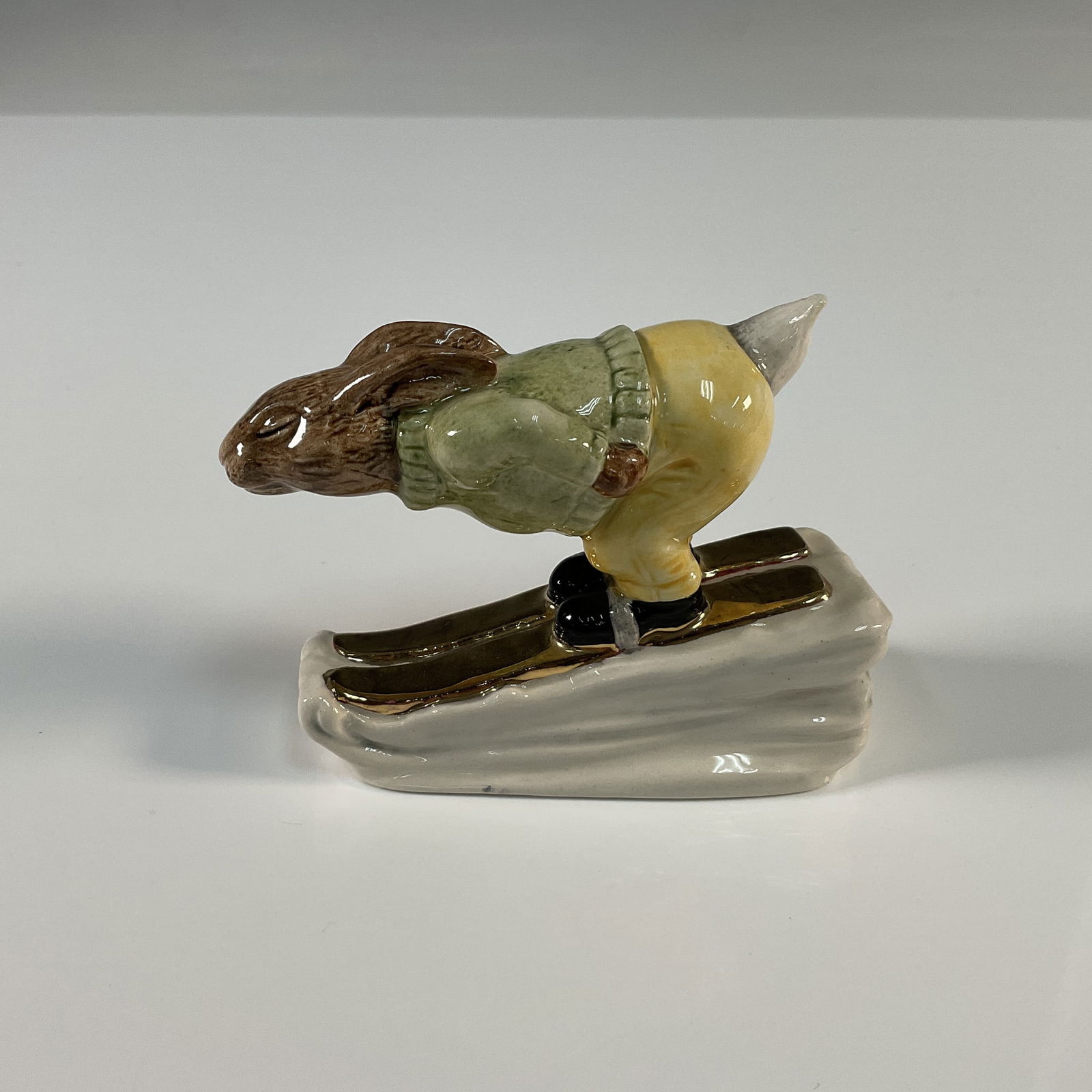 Royal Doulton Gold Colorway Bunnykins Figurine, Downhill: This delightful Royal Doulton Bunnykins figurine showcases a whimsical bunny in a downhill skiing pose. Hand painted in the rare gold colorway, this charming piece exudes playful energy and showcases