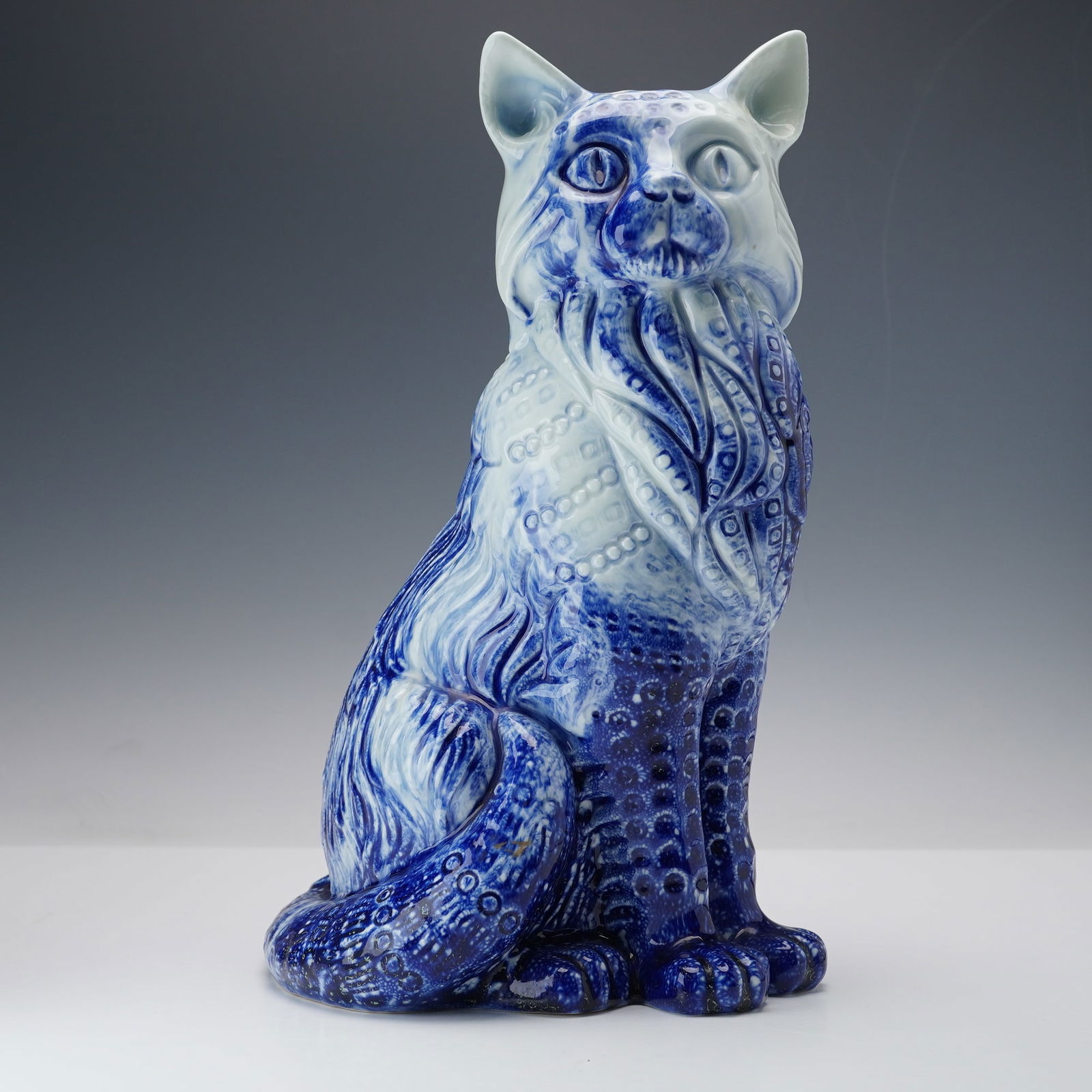 Royal Doulton Blue Flambe Veined Figurine,Large Cat: A sculpted porcelain feline rendered in the classic veined blue flambe glaze. The cat is modeled in a seated posture with deeply modeled fur and geometric relief texturing throughout the body. Royal