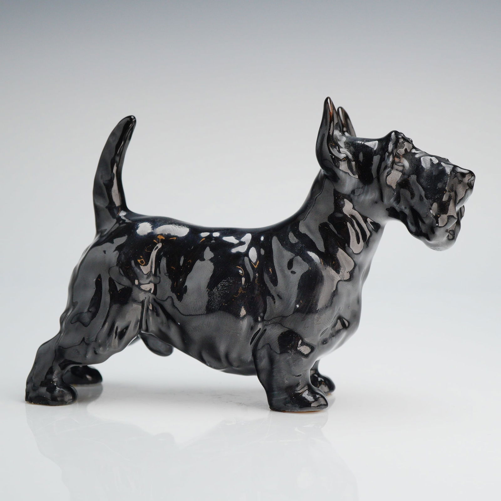 Royal Doulton Bone China Scottish Terrier Figurine: A Royal Doulton Bone China figurine depicting a Scottish Terrier (Scottie dog). The ceramic figurine is rendered in an alert, standing posture with the tail raised. It is finished with a high-gloss,