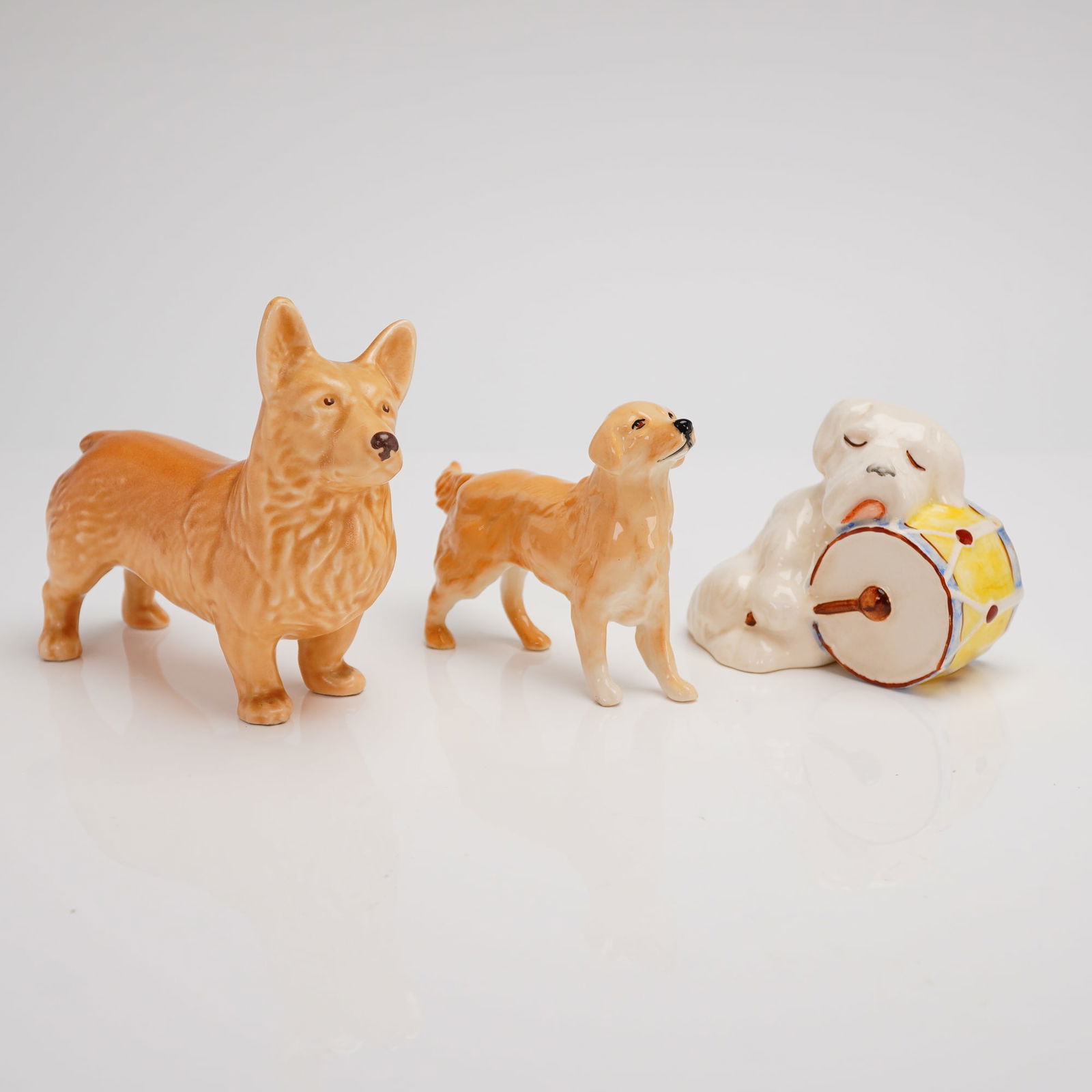 A Trio of Beswick Glazed Ceramic Dog Figurines: A collection of three glazed ceramic dog figurines manufactured by Beswick, England. The collection comprises three distinct figures, all finished with a high-gloss glaze typical of mid-20th-century