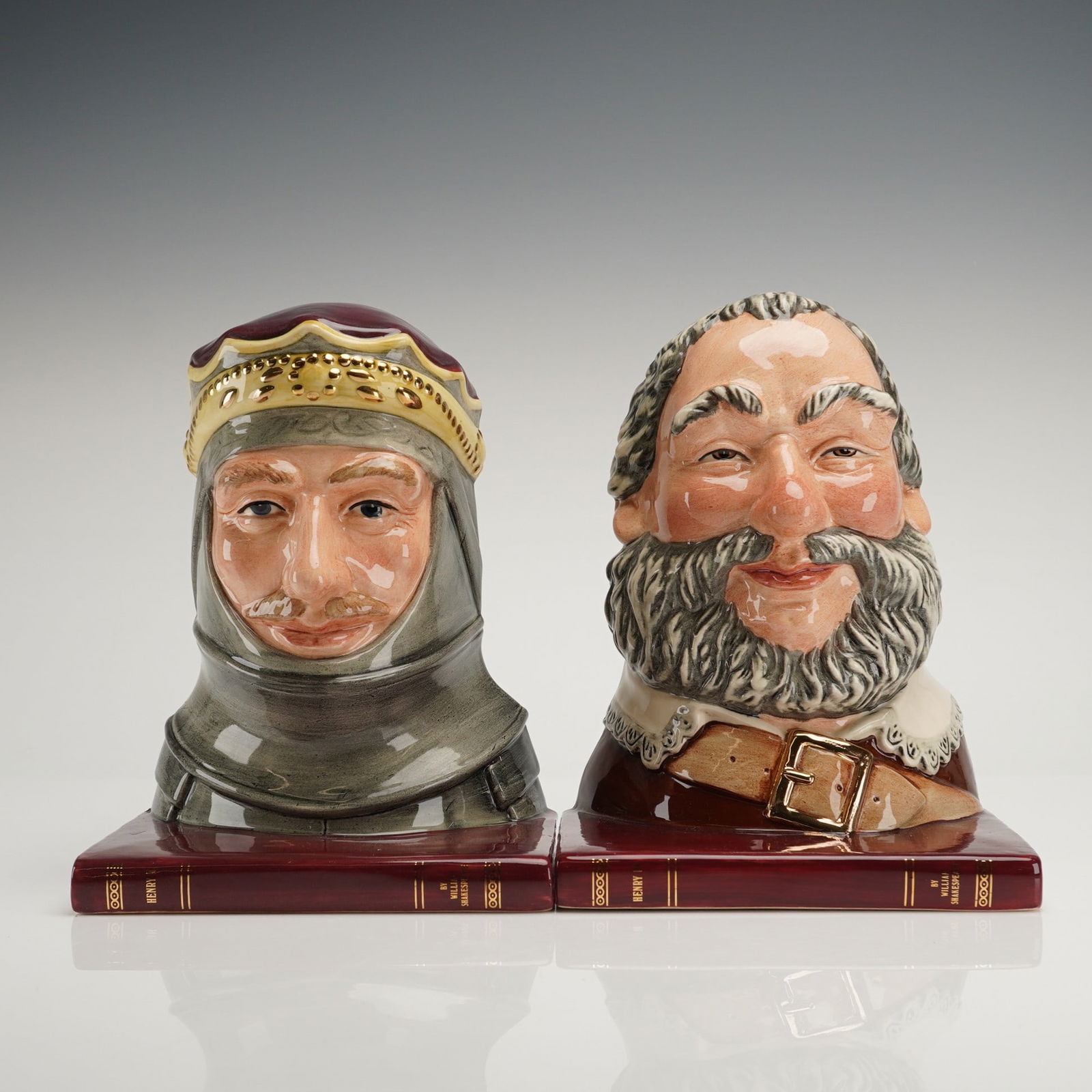 A Pair of Royal Doulton Porcelain Henry V and Falstaff Bookends: A pair of 2pc Royal Doulton porcelain bookends depicting the Shakespearean characters Henry V and Falstaff. Each character bust is mounted on a base modeled to resemble a maroon leather-bound book. He