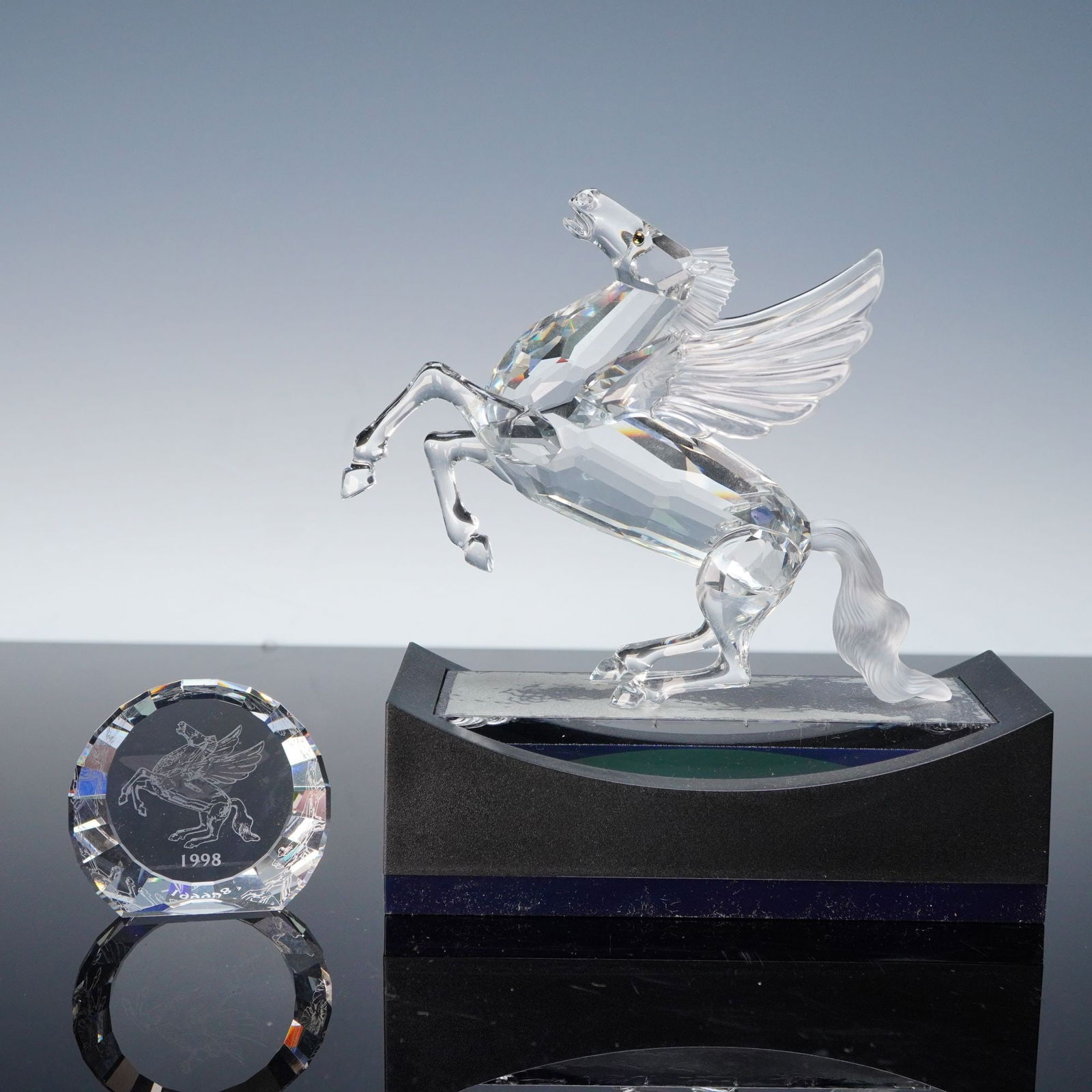 Swarovski 1998 Annual Edition Pegasus Figurine with Base and Plaque: A collection of five items comprising the Swarovski Crystal Society (SCS) 1998 Annual Edition figurine, titled "Pegasus," along with its associated accessories. The central piece is a multi-faceted, c