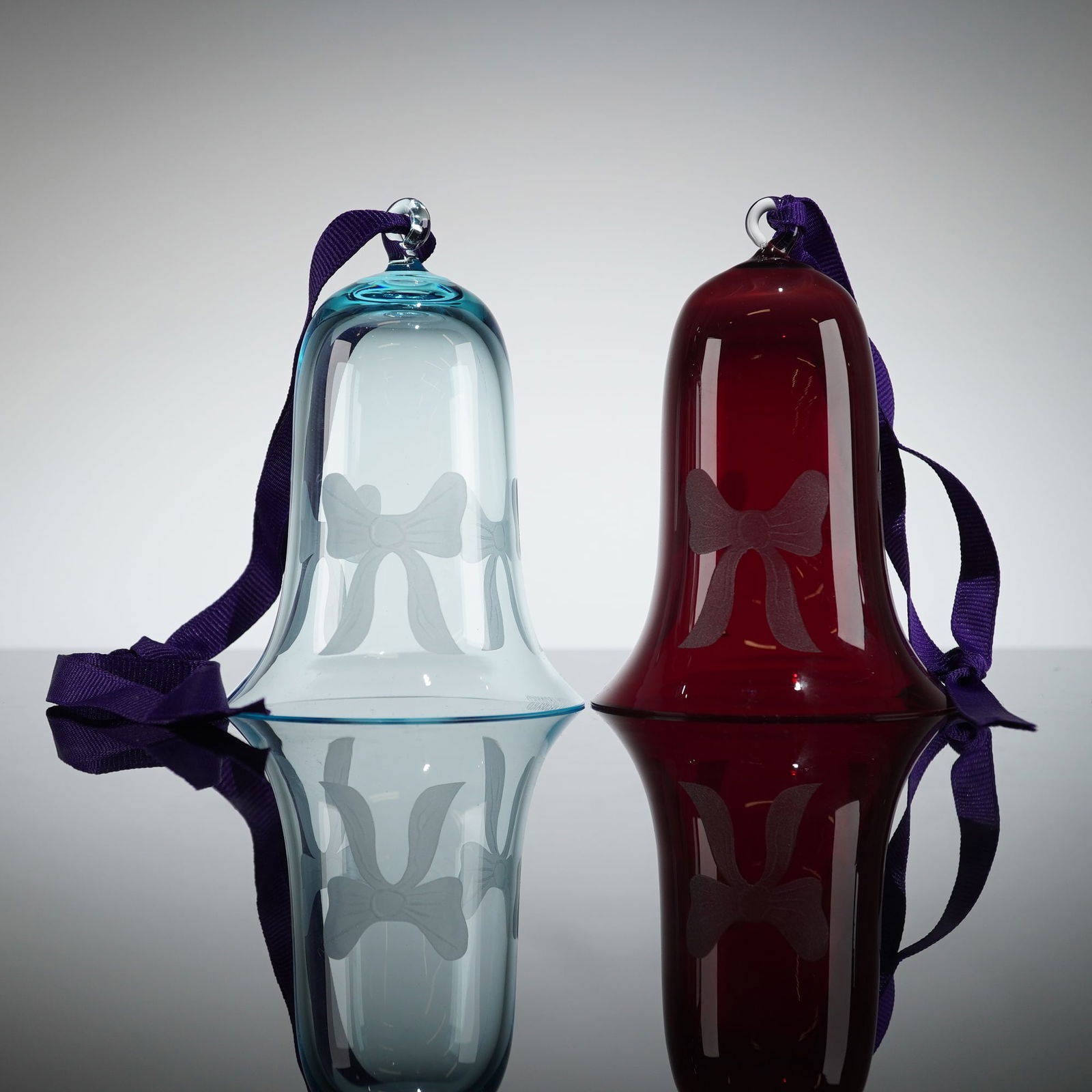 Pair of William Yeoward Crystal Bell Ornaments, Red and Blue: Ornaments featuring one transparent turquoise blue bell and one transparent ruby red bell. These 2pc crystal ornaments are crafted from hand-blown crystal glass with a flared silhouette, designed for