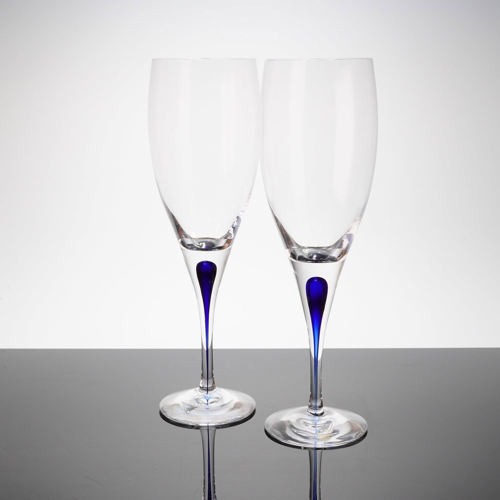 A Pair of Orrefors Intermezzo Blue Claret Wine Glasses: A pair of Orrefors Intermezzo Blue stemmed claret wine glasses, designed by Erika Lagerbielke. Each glass is crafted from clear crystal, featuring a tall, slender stem and a conical bowl. The defining
