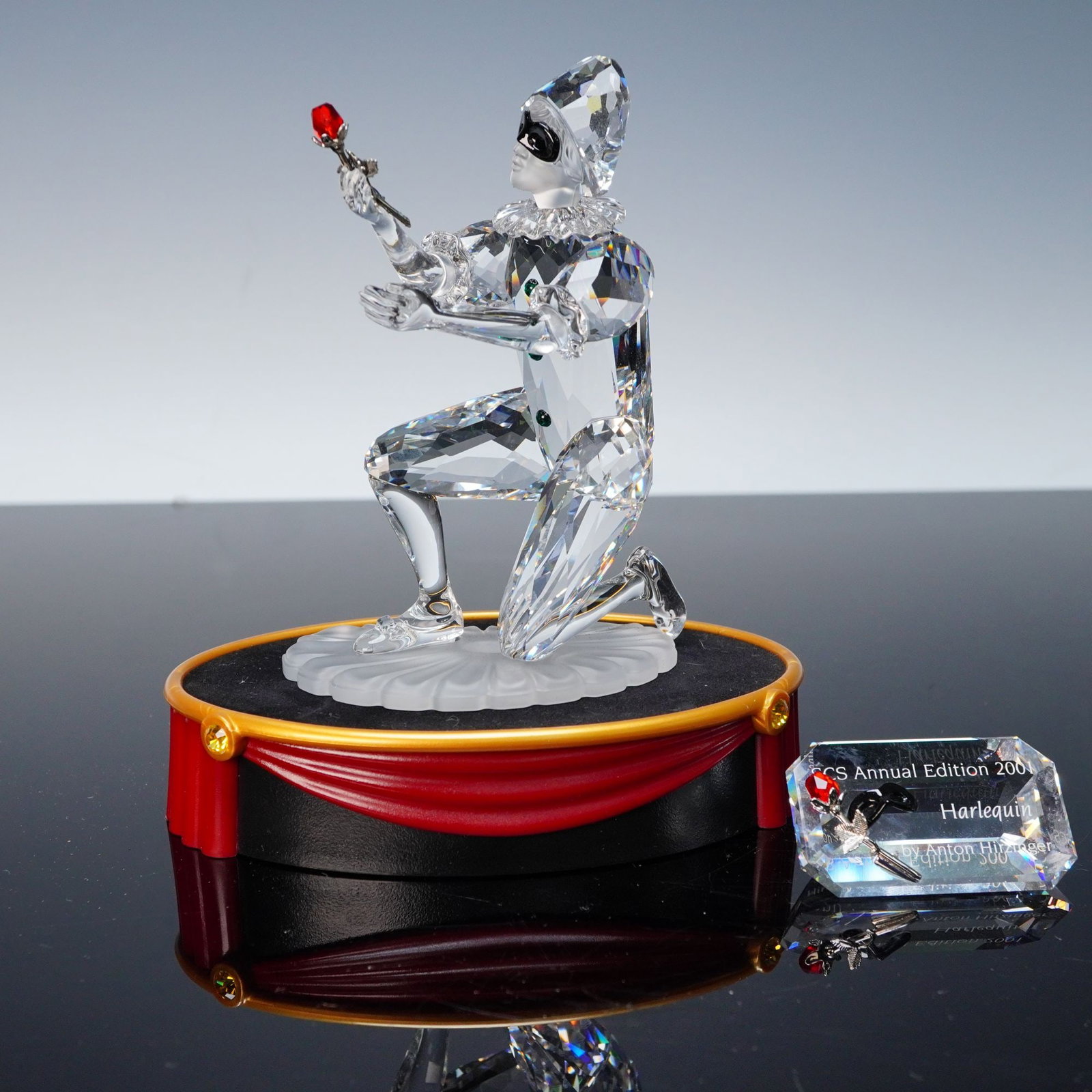 Swarovski SCS Annual Edition 2001 Harlequin with Plaque and Display Base: A collection of items comprising the Swarovski SCS Annual Edition 2001 Harlequin figurine, its accompanying display base, identification plaque, and original presentation box. This Annual Edition piec