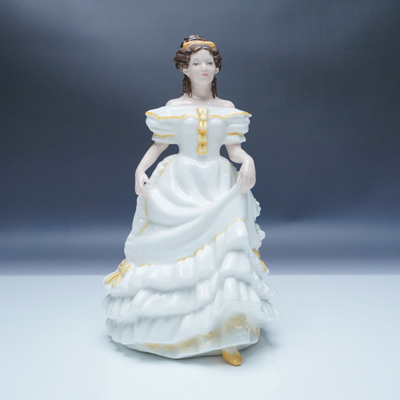 Royal Doulton Figurine Angela HN3690: This exquisite Royal Doulton figurine, Angela HN3690, showcases a beautifully detailed young woman in a flowing white gown adorned with delicate golden accents. Crafted from fine bone china, this eleg