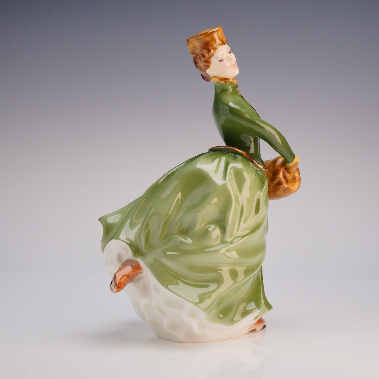 Royal Doulton Figurine Grace HN 2318: The figure is hand-painted and finished in a high-gloss glaze, depicting a woman in a dynamic, skating-like pose. She is dressed in a green bodice and a flowing skirt, which is green externally and wh
