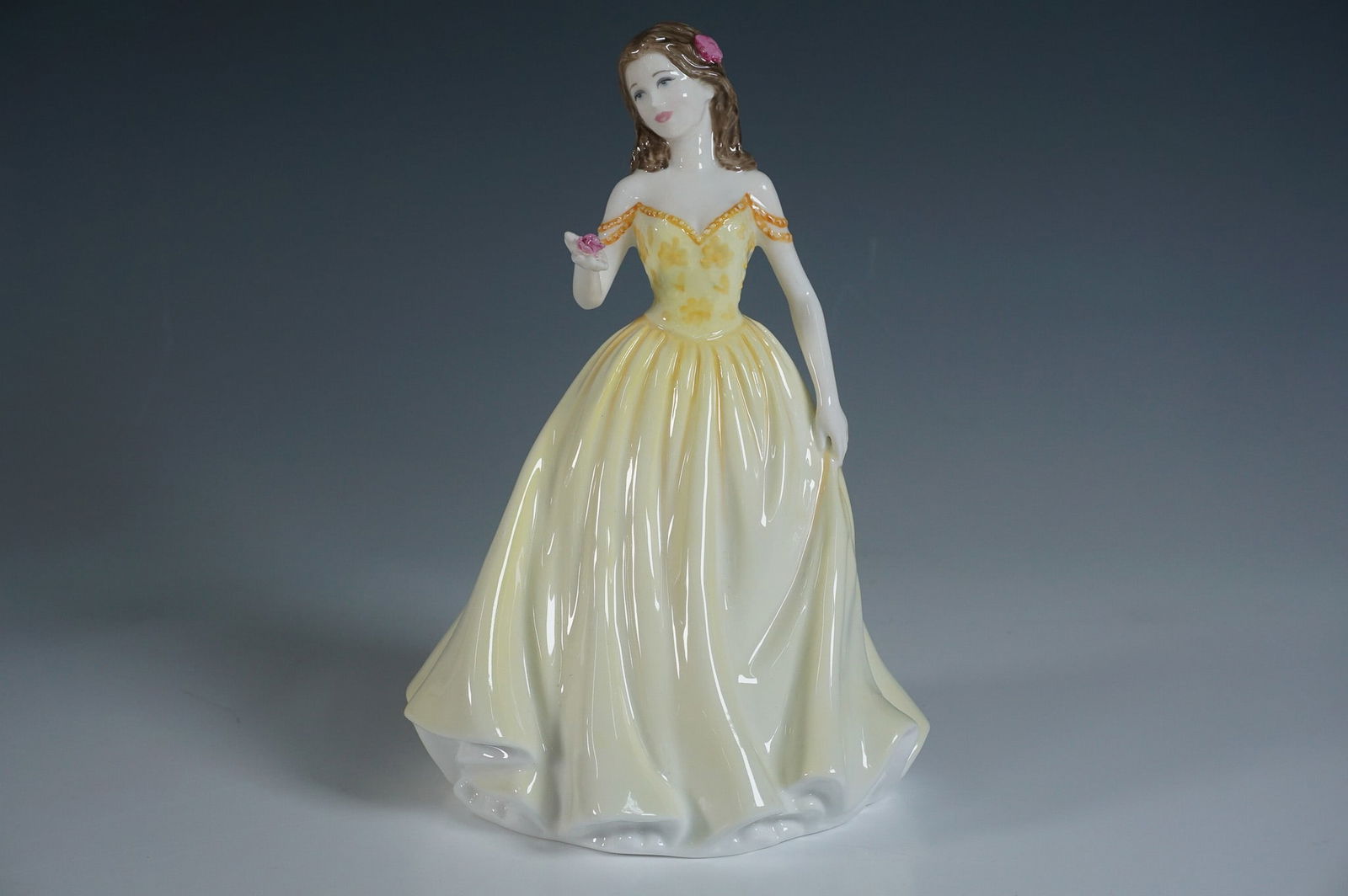 Royal Doulton Figurine, Rose HN4581: This exquisite Royal Doulton figurine is part of the Classics Series and a Michael Doulton Exclusive from 2004. Handcrafted in fine bone china, it features a young lady in a flowing yellow gown with d