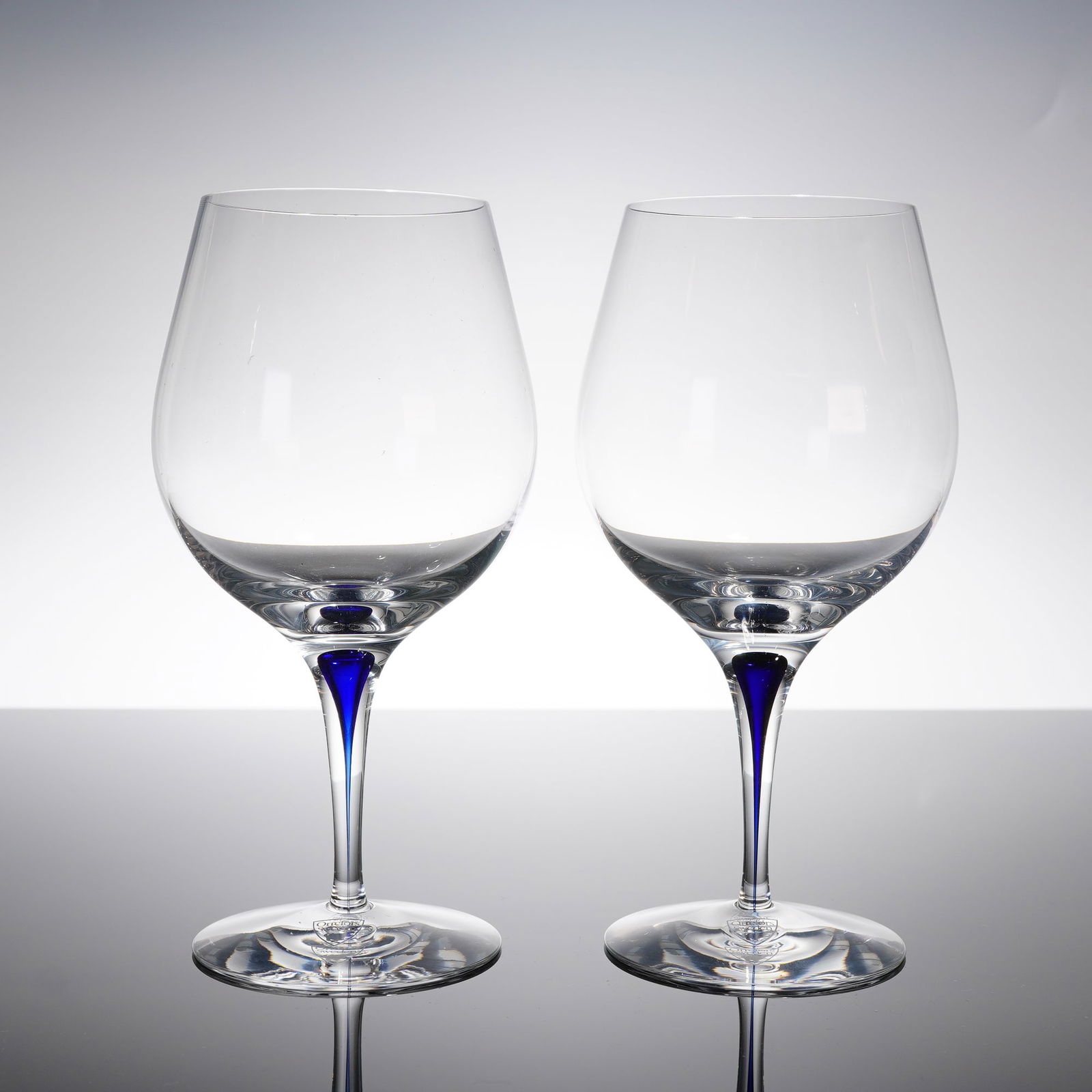 A Pair of Orrefors Intermezzo Wine Glasses: A pair of Orrefors Intermezzo Blue stemmed glasses. This 2pc set is constructed of clear crystal, featuring a tall, broad bowl suitable for various wines, including use as a versatile fi?uted champagn