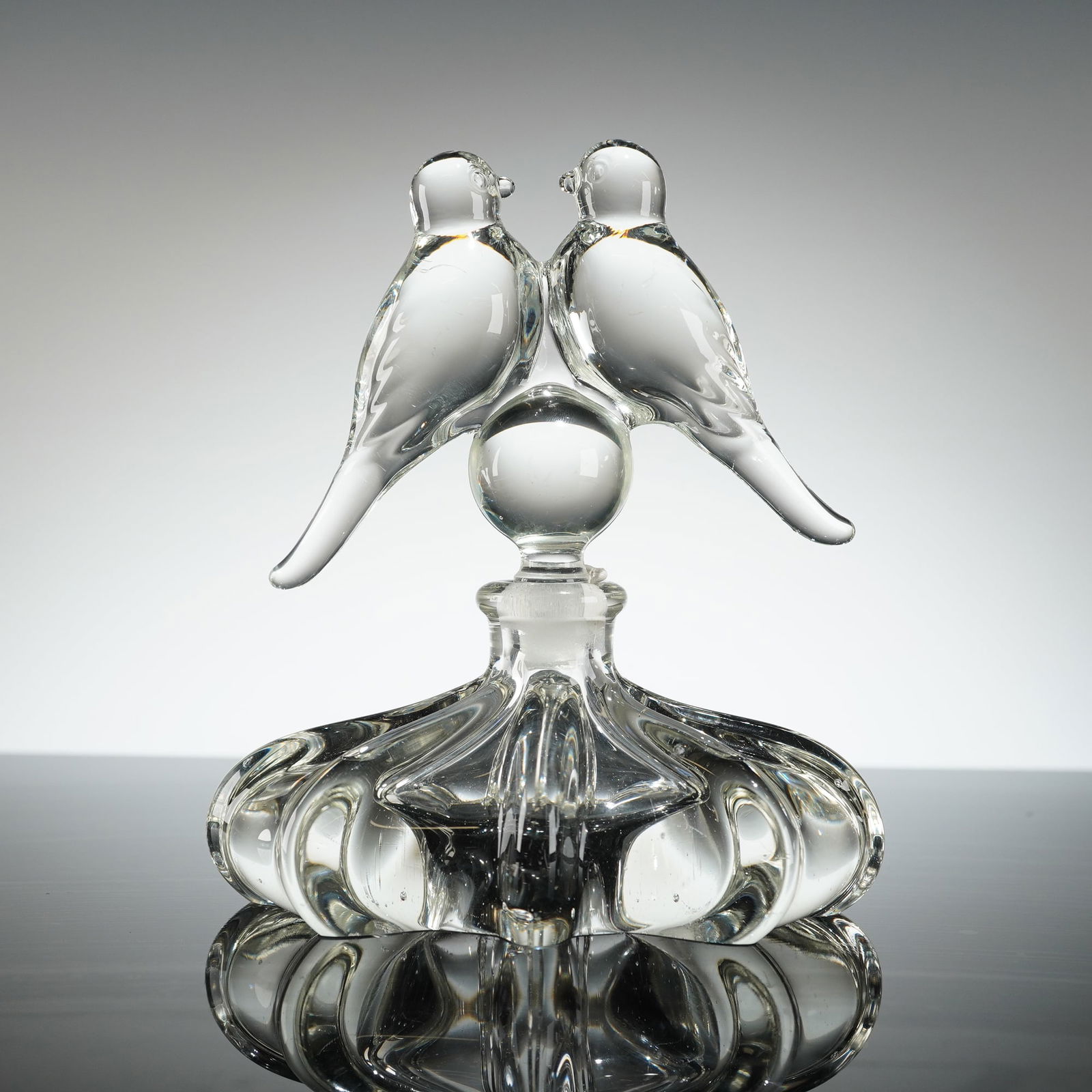 Gundersen Pairpoint Crystal Perfume Bottle with Lovebirds Stopper: This two-piece set comprises the bottle body and the figural stopper. The bottle material is clear, colorless, heavy molded glass. The body features a squat, globular form with deep vertical fluting o