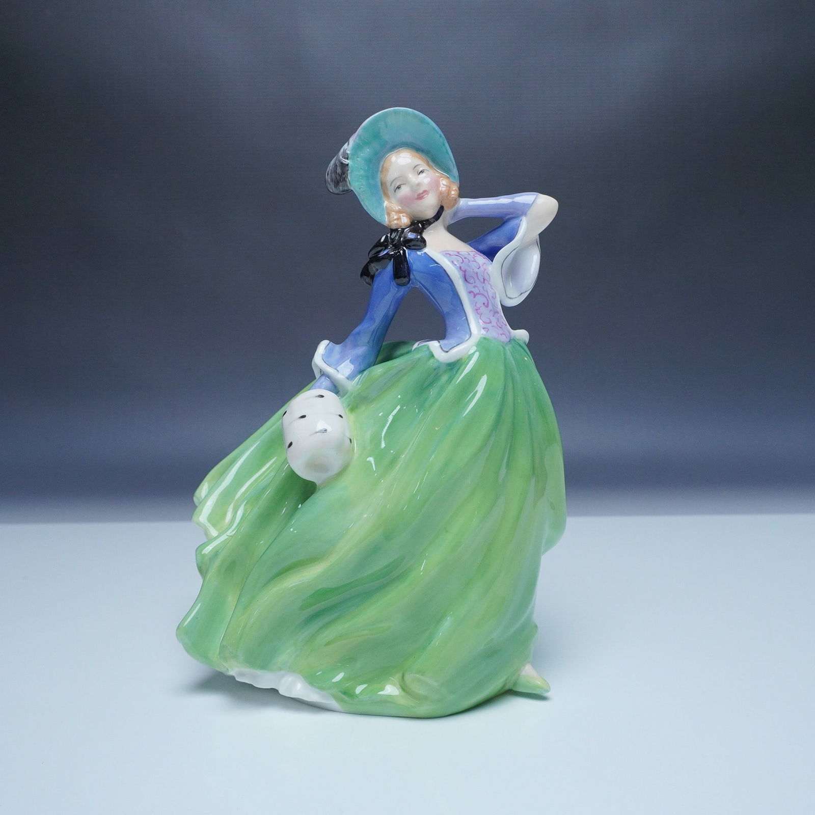 Royal Doulton Autumn Breezes Figurine HN1913: This is a Royal Doulton figurine titled Autumn Breezes, model number HN1913. The piece depicts a graceful young woman in a flowing green skirt and blue jacket, with a bonnet and muff, embodying the es