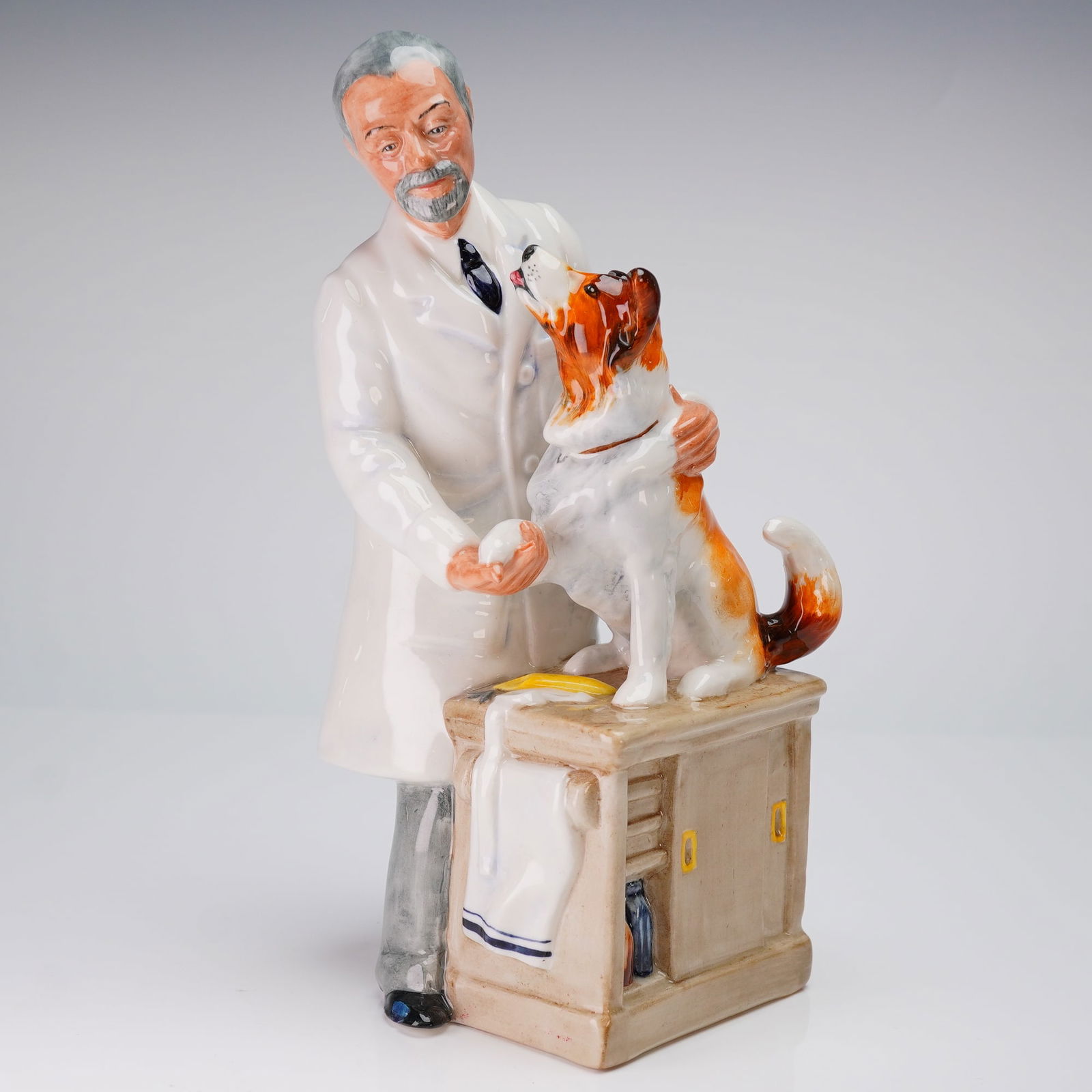 Royal Doulton Figurine Thanks Doc! HN2731: A Royal Doulton figurine titled Thanks Doc! HN2731, executed in glazed ceramic. This composition depicts a veterinarian wearing a white lab coat and grey trousers, interacting with a tricolor dog that