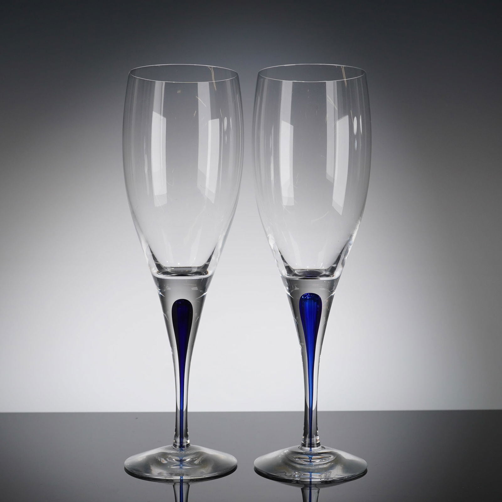 A Pair of Orrefors Intermezzo Blue Crystal Champagne Flutes: A pair of contemporary Orrefors Intermezzo Blue crystal glasses. These items are executed in blown clear crystal glass, designed as tall champagne fi?utes with slender bowls and tapered stems. The sig