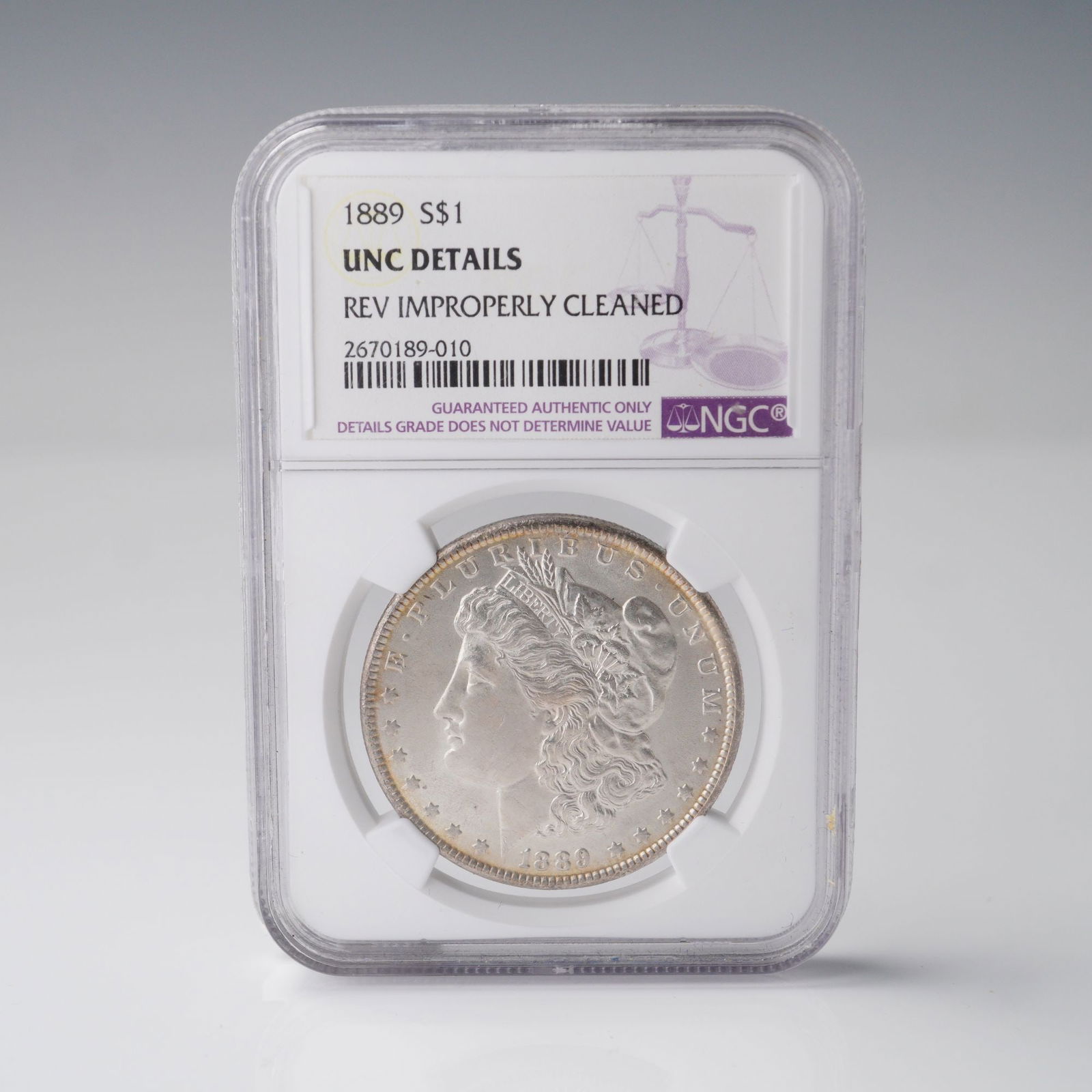 1889 Morgan Silver Dollar Coin UNC Details Rev Improperly Cleaned NGC: The obverse of the 1889 Morgan Silver Dollar coin features a left-facing bust of Liberty with her hair flowing beneath a Phrygian cap, a symbol of freedom. The word LIBERTY appears on her headband, an