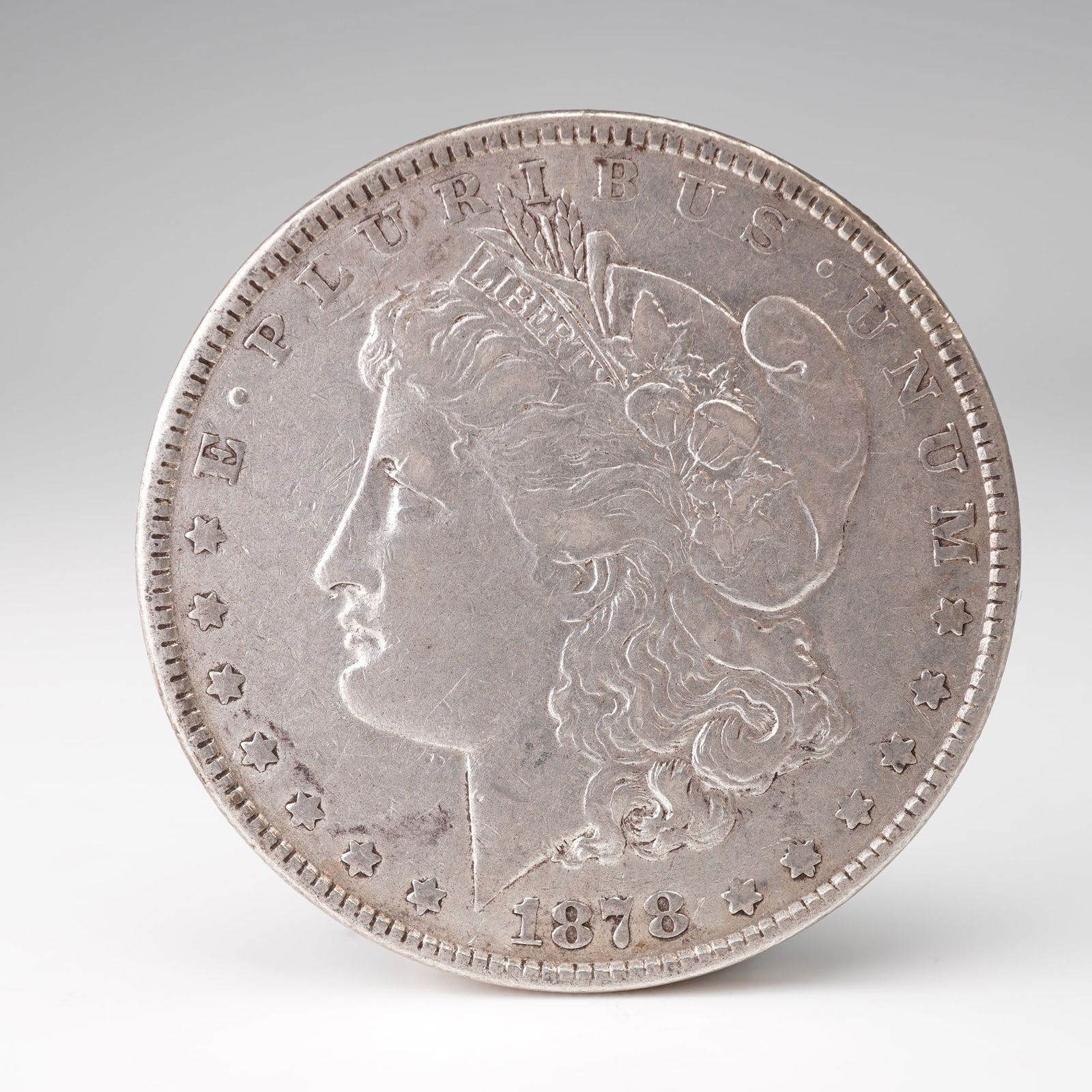 1878 Morgan Silver Dollar 7 Tail Feathers Reverse: 1878 Morgan Silver Dollar featuring the early 7 Tail Feathers reverse, designed by George T. Morgan. The obverse depicts Liberty wearing a Phrygian cap adorned with cotton and wheat, symbolizing