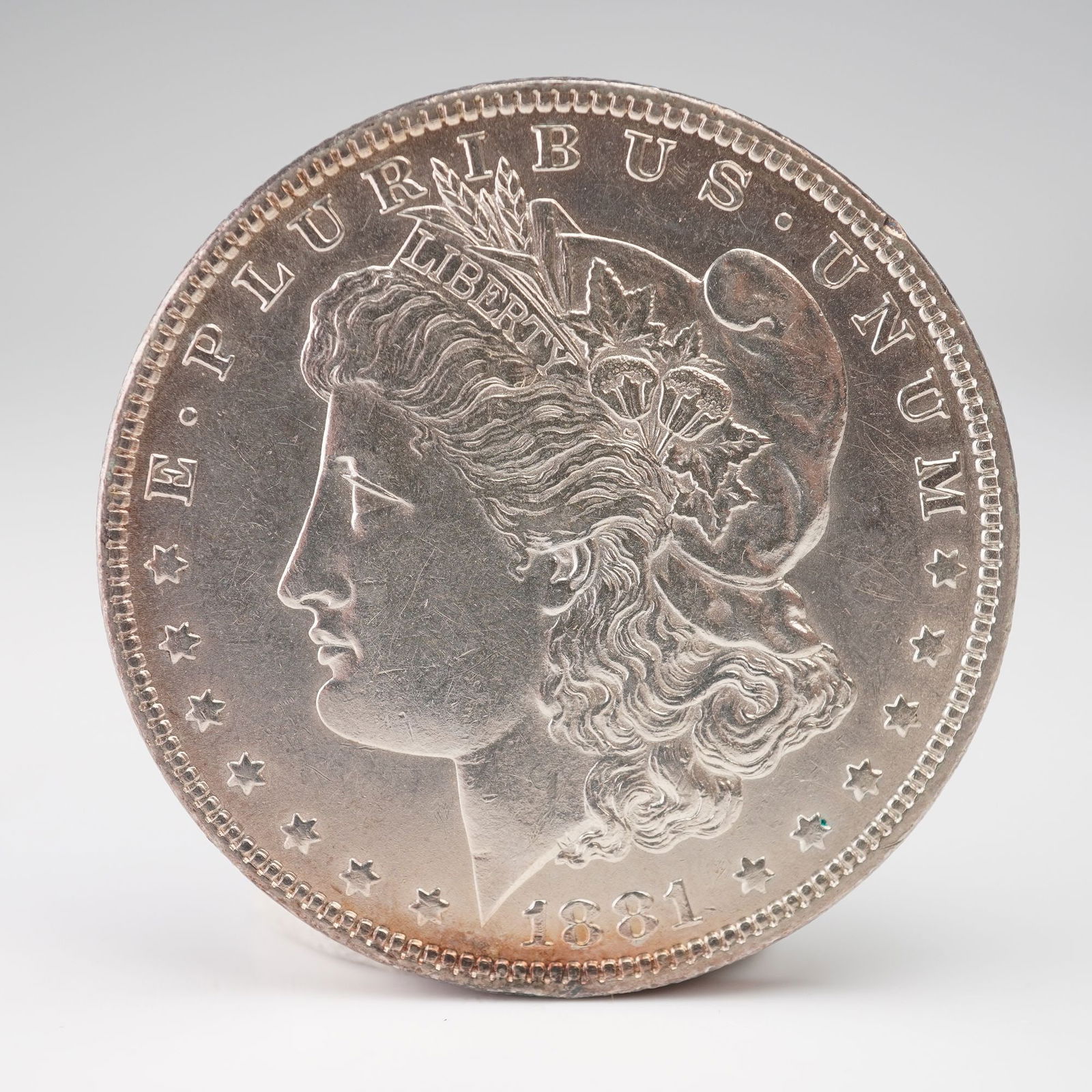1881-O Morgan Silver Dollar: An 1881-O Morgan Silver Dollar struck at the New Orleans Mint. The obverse bears the classic bust of Liberty adorned with a Phrygian cap and a wreath of cotton and wheat, along with E PLURIBUS UNUM an