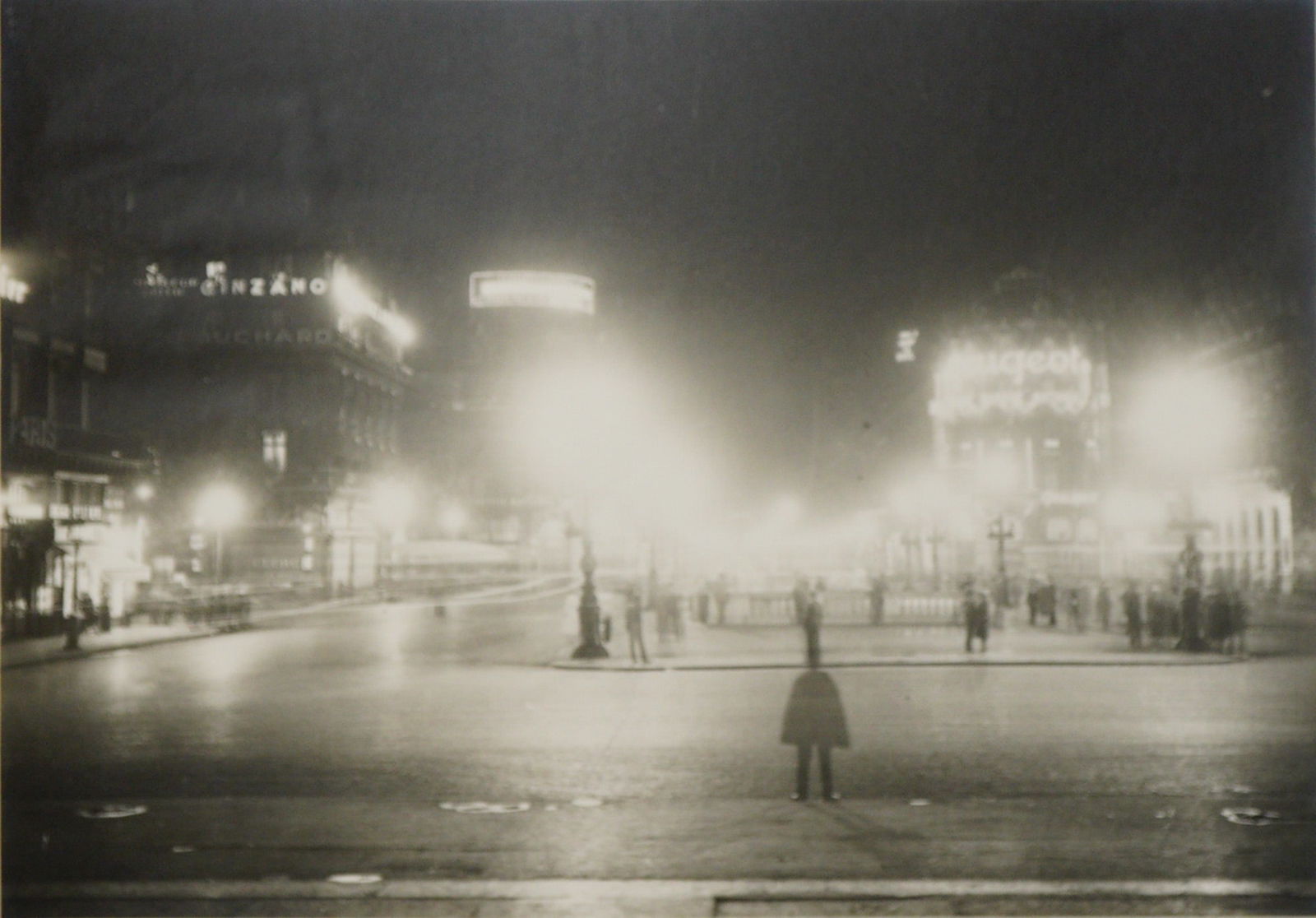 French Gelatin Silver Print Paris 1925 Place de l'Opera Night: A gelatin silver print on board depicting a dramatic urban night scene of the Place de l'Opera in Paris. The image utilizes long exposure techniques to capture the movement of traffic and figures, ren