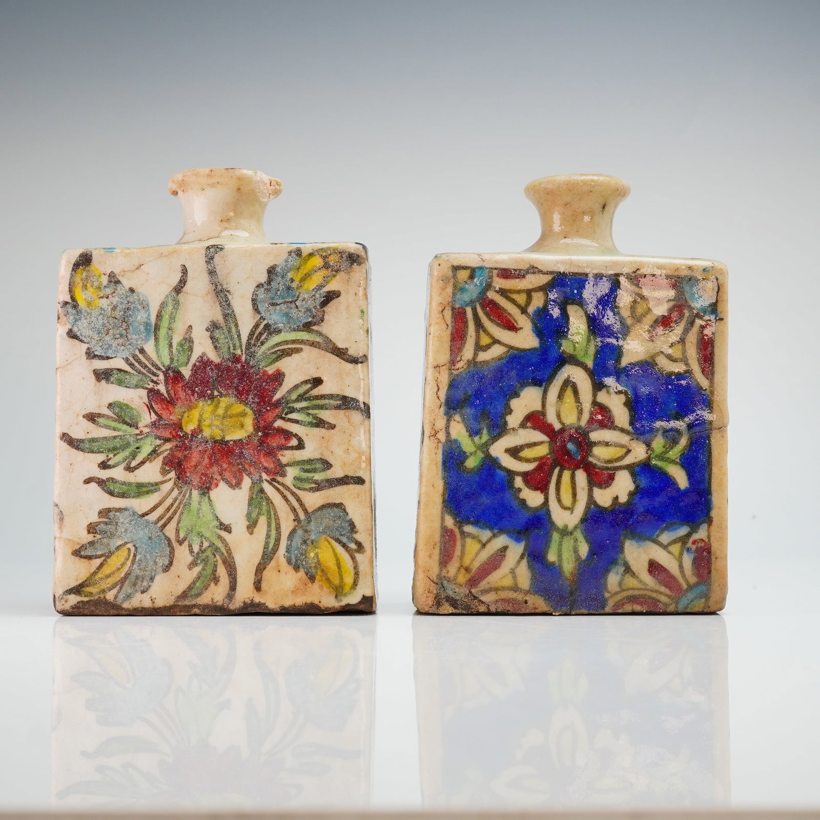 2pc Antique Persian Qajar Iznik Pottery Bottles, Floral Design: Bottles attributed to the Qajar period, decorated in the Iznik-inspired floral style. Each squared-form bottle features hand-painted floral compositions with scrolling leaves and blossoms, executed in