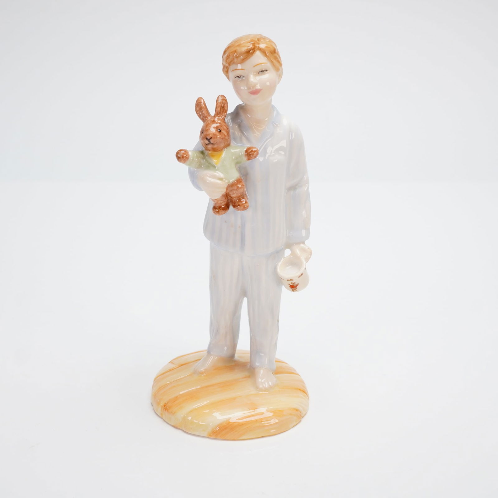 Royal Doulton Figurine, Lights Out HN4465: A glazed bone china figurine by Royal Doulton, titled Lights Out HN4465. This piece depicts a young boy dressed in light blue and white striped pajamas, standing on an orange-tan stylized base. The bo