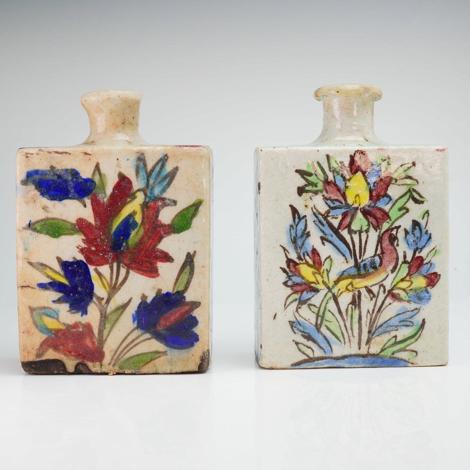 2pc Antique Persian Qajar Iznik Pottery Bottles: Bottles attributed to the Qajar period and decorated in the Iznik-inspired style. Each bottle of squared form with short neck and flared rim, hand-painted with stylized floral and foliate motifs rende
