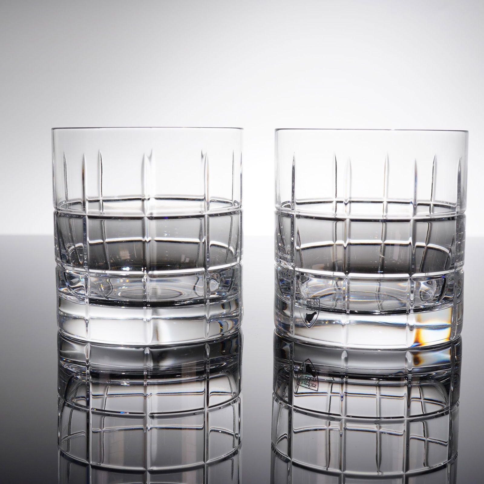 A Pair of Orrefors Street Double Old Fashioned Crystal Glasses: A pair of Orrefors Street Double Old Fashioned crystal whiskey glasses. Each tumbler features a heavy, clear cylindrical body with a thick base. The decoration consists of a classic geometric cut pate
