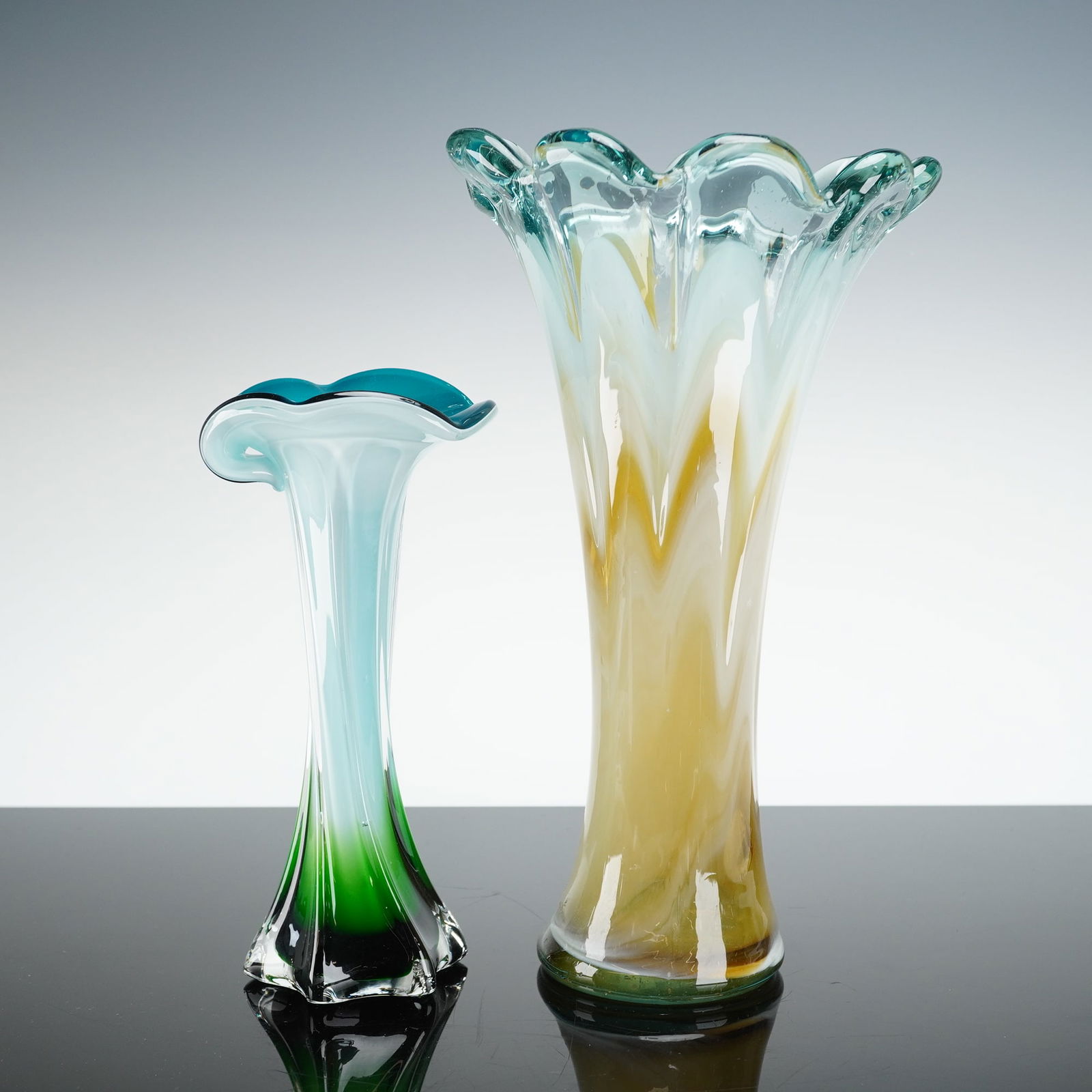 2pc Art Glass Vases with Ruffled Rims, Blue, Green, and Amber Tones: Two art glass vases featuring elongated trumpet forms with softly ruffled rims, each displaying distinct color treatments. The taller example exhibits flowing opalescent white glass with warm amber an