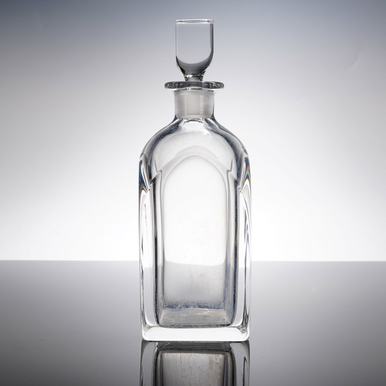 A Mid-Century Crystal Brandy Decanter with Stopper: A heavy crystal brandy decanter atributed to Orrefors, consistent with Mid-Century Modernist design principles. The rectangular body features substantial vertical concave cut or molded arches