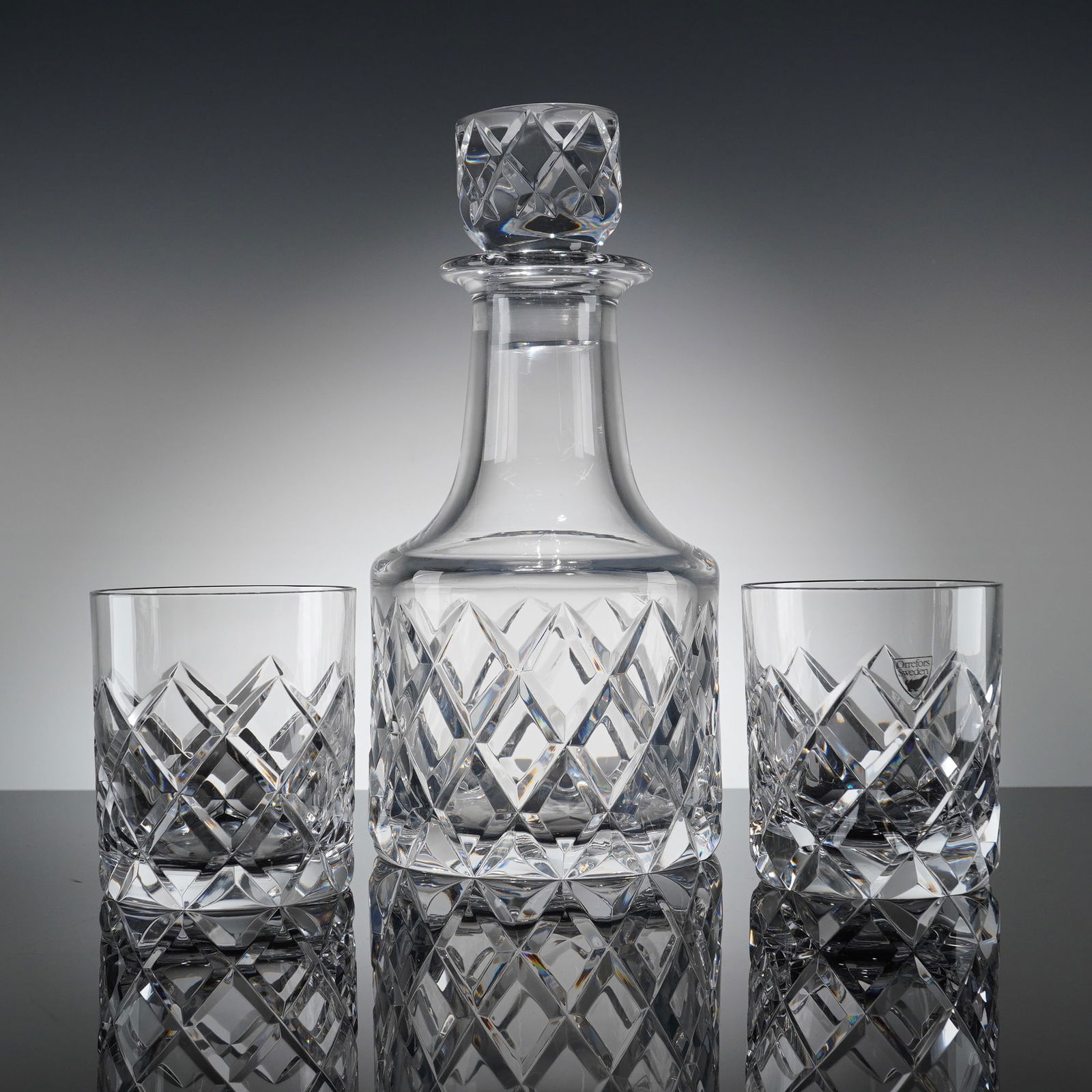 3pc Orrefors Sofiero Cut Crystal Decanter with Stopper: A cut crystal decanter and matching cylindrical stopper, identified through market consensus as the Sofiero patern produced by Orrefors. The decanter features a broad, round base tapering up to a