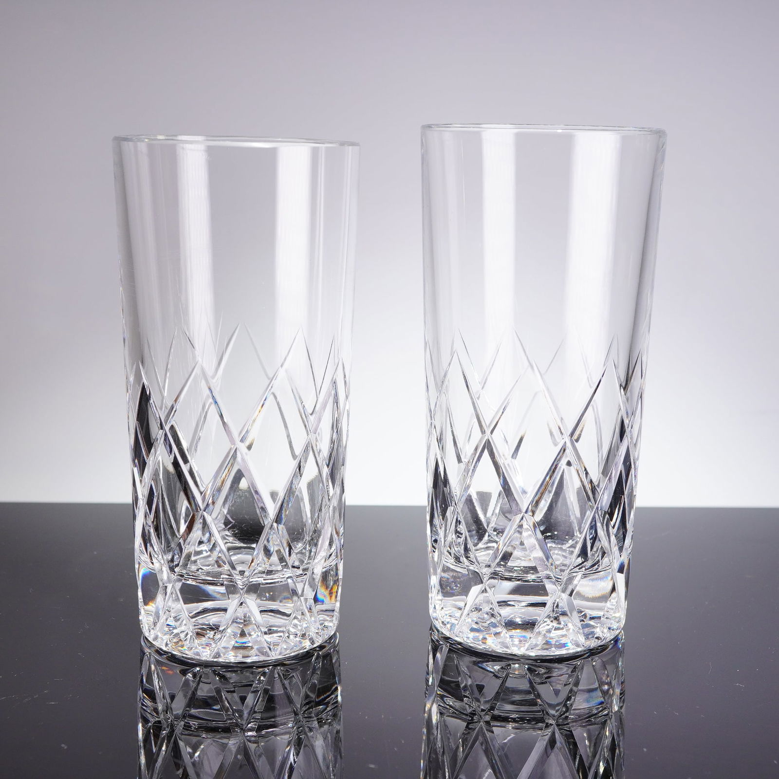 A Pair of Orrefors Sofiero Patern Cut Crystal Highball Glasses: A pair of cylindrical highball glasses atributed to Orrefors in the Sofiero patern. These heavy vessels are crafted from clear cut crystal or high-quality glass. The lower half of the body and the