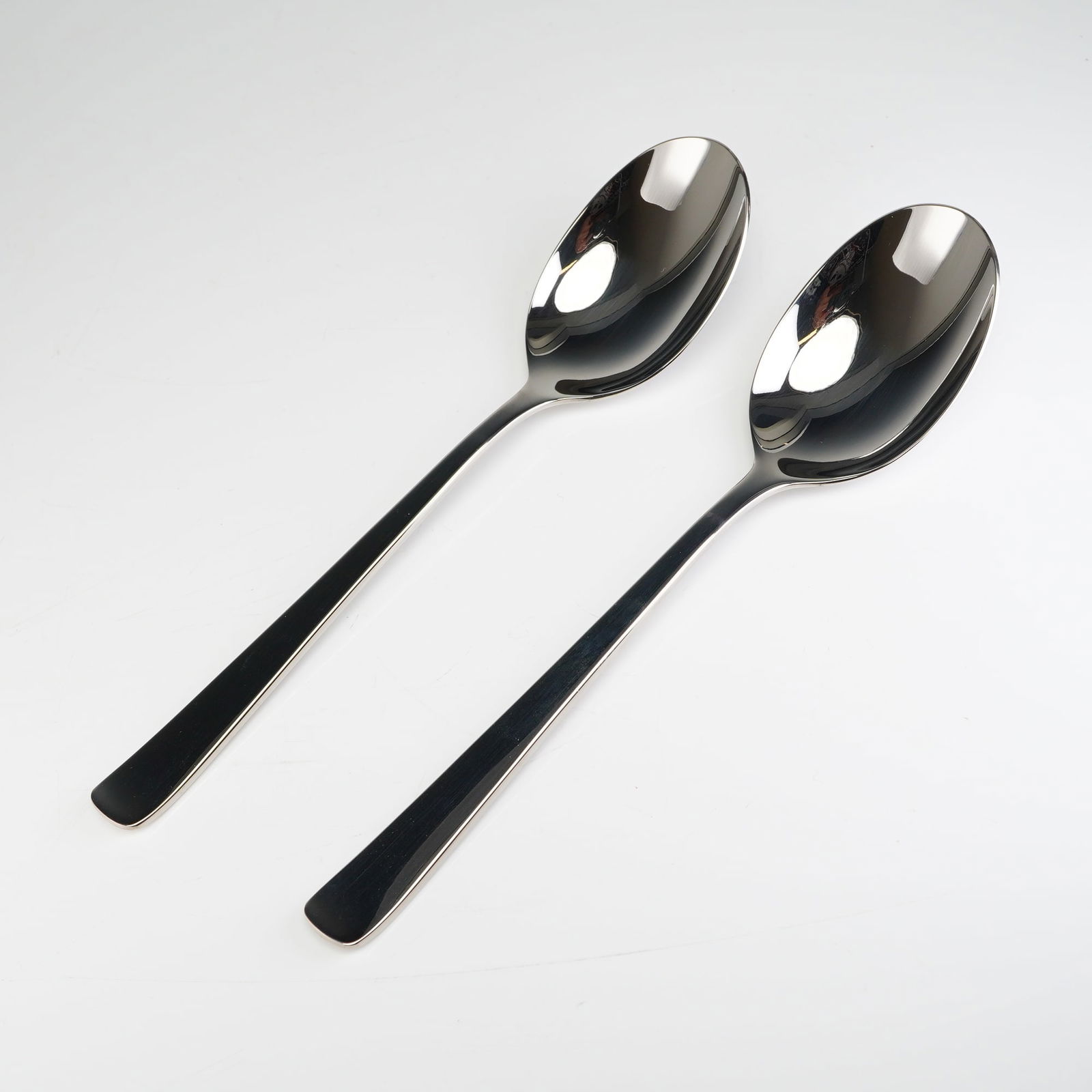 2pc Robbe & Berking Stainless Steel Serving Spoons: These items exhibit a contemporary, minimalist design with long, slender handles and deep oval bowls, suitable for use as soup or bouillon spoons. The material is identified as polished stainless stee