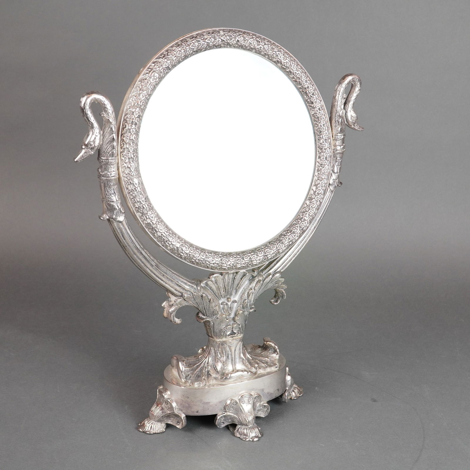 Neo-Classical Revival Silver-Plated Vanity Mirror Swan Finials: A single ornate mirror constructed from heavily cast silver-plated base metal, presented in a Neo-classical or revival style. The piece functions as a tabletop dressing or vanity mirror, featuring a c