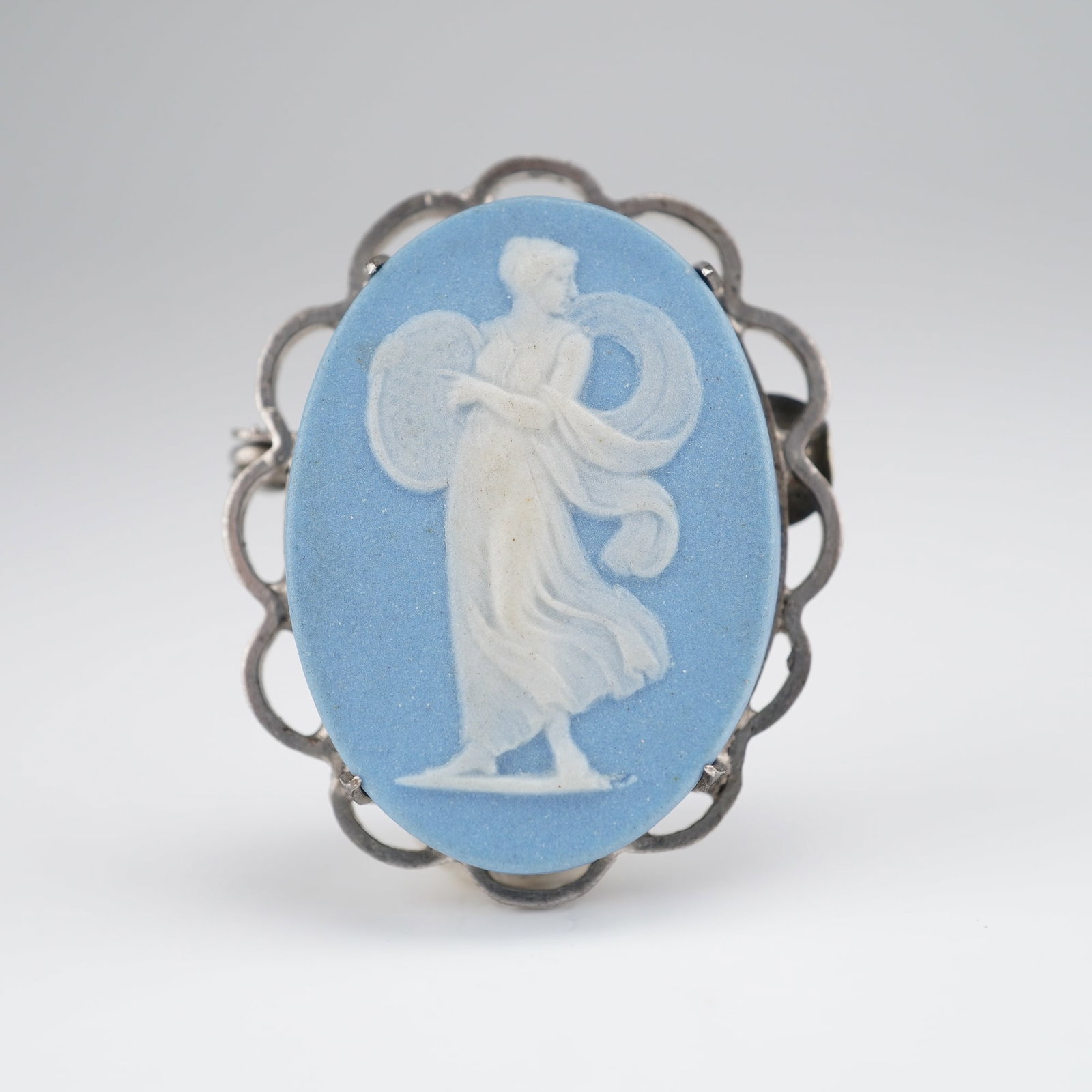 Wedgwood Sterling Silver Blue and White Jasperware Cameo Brooch: A vintage Wedgwood blue and white jasperware cameo brooch set in a sterling silver frame. The oval ceramic plaque features a pale blue ground with a white bas-relief depicting a classical winged