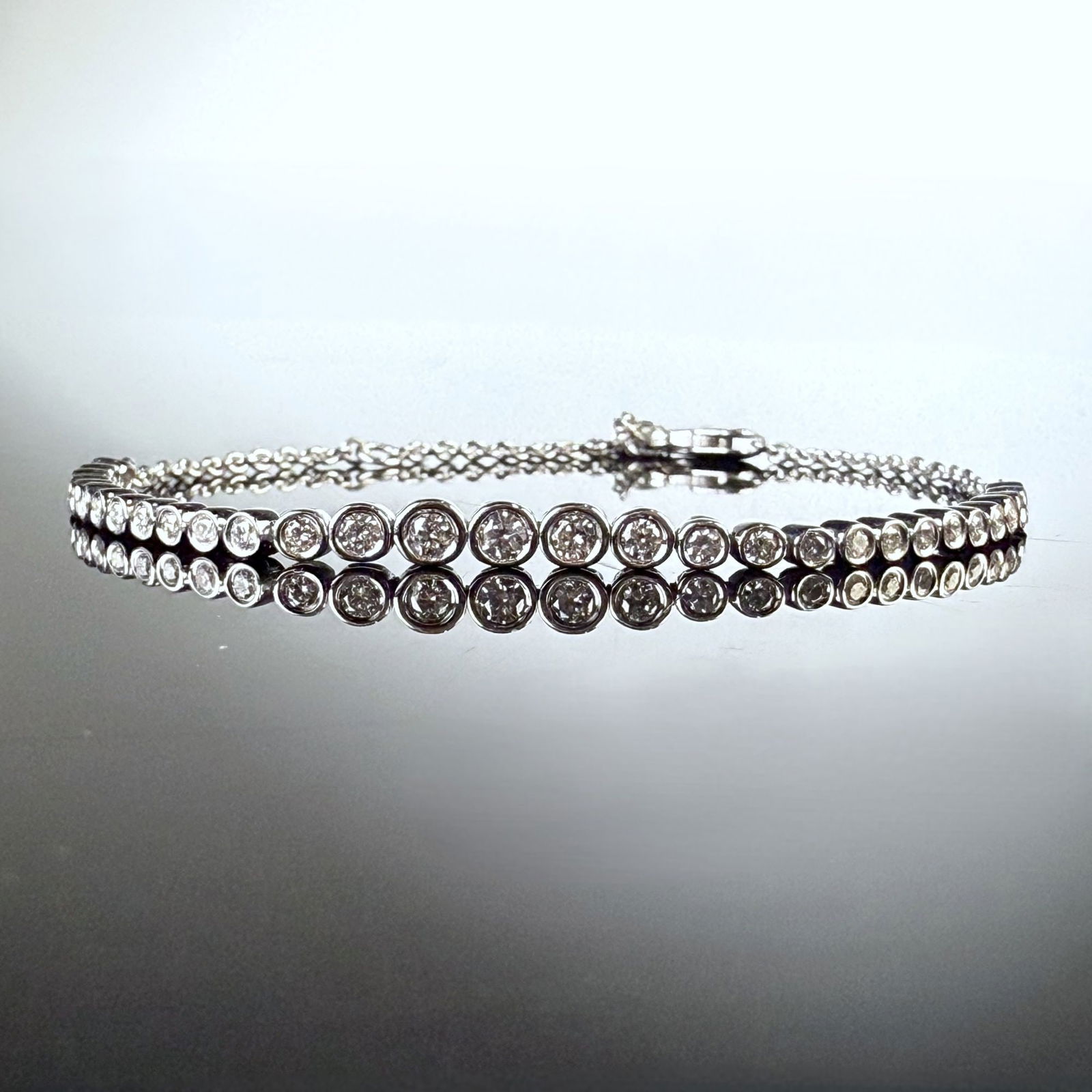 14K White Gold and 0.48ctw Round Diamond Bezel Tennis Bracelet: A contemporary 14K white gold bracelet featuring a graduating row of round brilliant-cut diamonds with a total weight of 0.48ctw. Each gemstone is secured within an individual polished bezel setting.