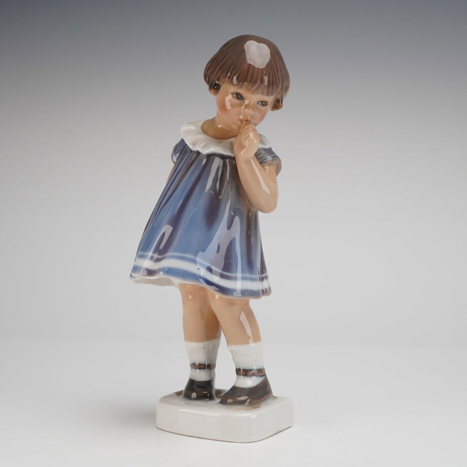 Dahl Jensen Porcelain Figurine No. 1026, Little Girl 'Gutte': A Dahl Jensen figurine, model number 1026, often known as 'Gutte' or 'Little Girl Figurine'. The figure depicts a young girl standing on a rectangular plinth, rendered in a shy or thoughtful pose with