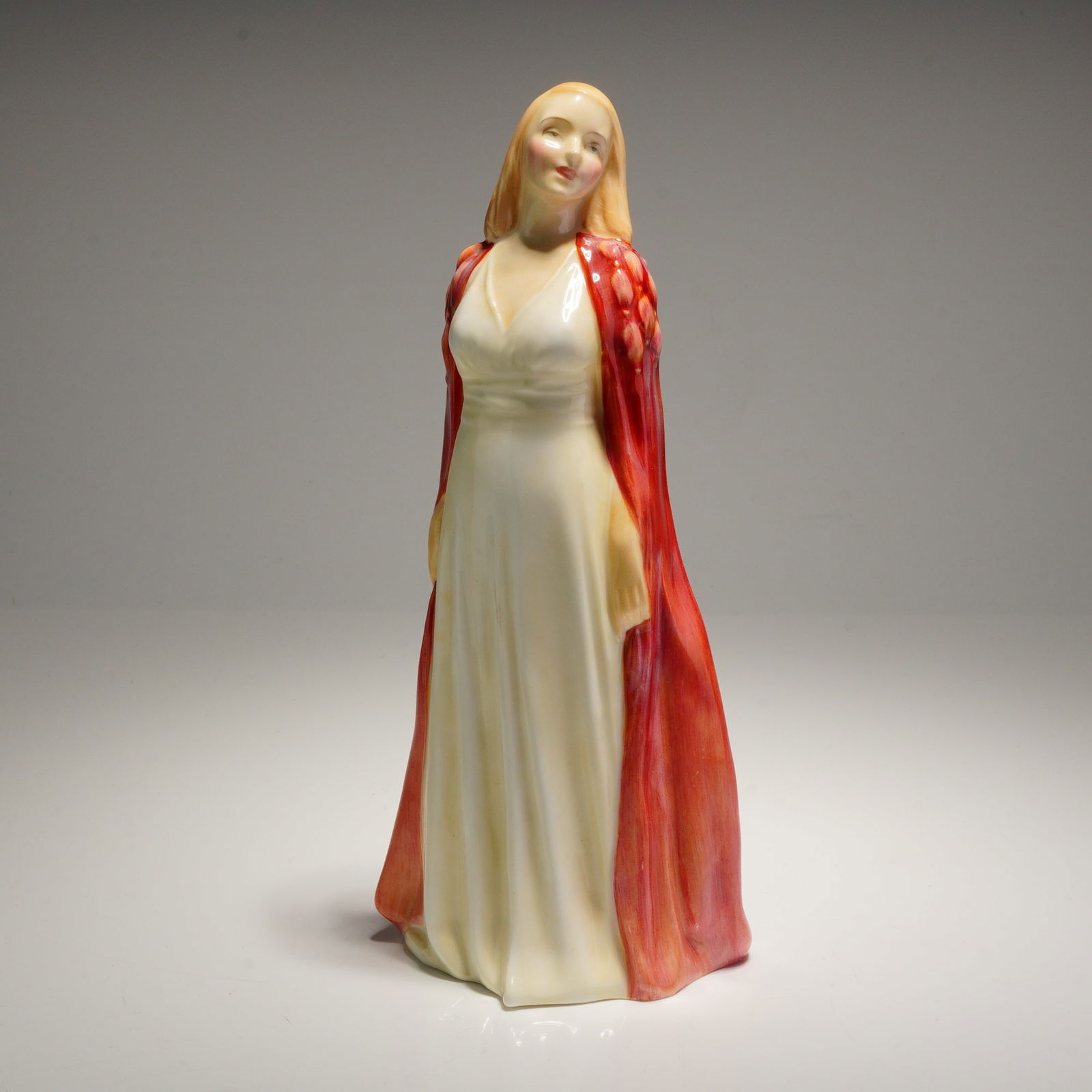 Royal Doulton Figurine Collinette HN 1999: A glazed bone china figurine, Collinette (HN1999), depicting a woman in a cream dress and a flowing red and orange cloak. The underside features the Royal Doulton backstamp, the title, and the model n