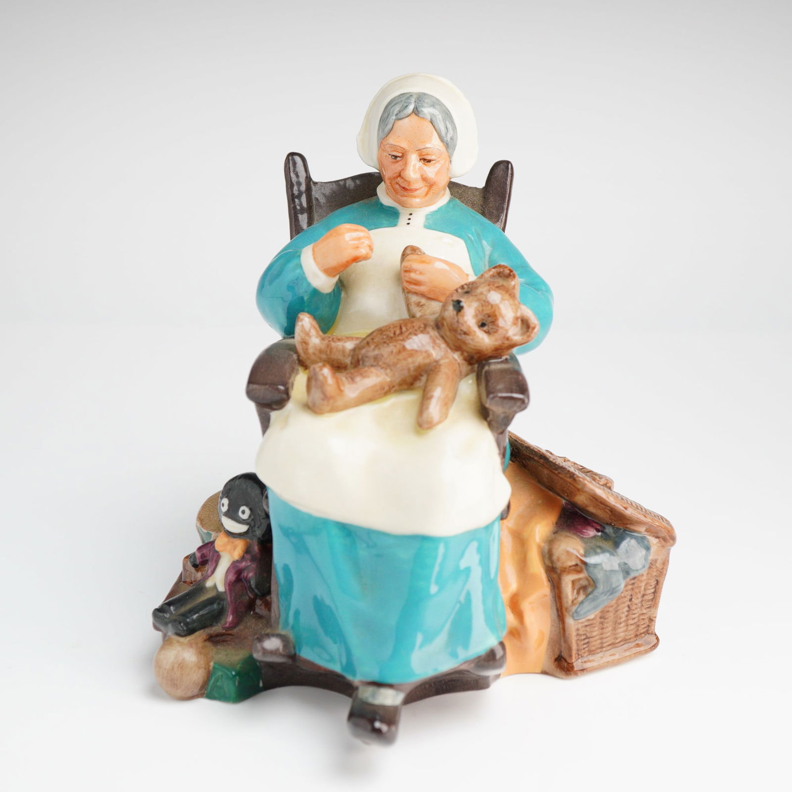 Royal Doulton Nanny Figurine HN 2221: A single glazed porcelain figurine by Royal Doulton, titled Nanny, model number HN 2221. The figure depicts an elderly woman seated in a brown rocking chair, dressed in a blue-green gown and white apr