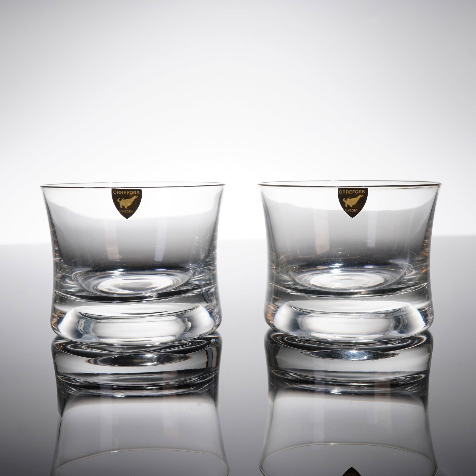 A Pair of Orrefors Crystal Old Fashioned Glasses: A pair of Orrefors crystal whiskey glasses, also known as Double Old Fashioned tumblers. These 2pc glasses are characterized by a heavy, thick base and slightly curved, clear crystal sides, adhering t