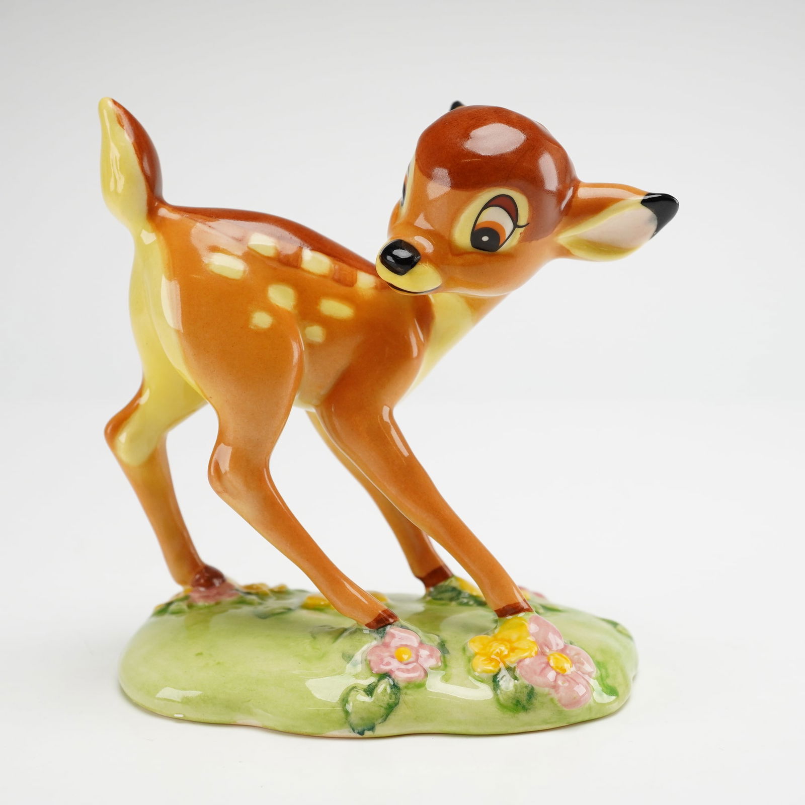 Royal Doulton Disney Figurine, Bambi FC1: This hand-decorated porcelain figurine depicts the character Bambi standing on a grassy base accented with pink and yellow flowers, finished with a high-gloss glaze. The underside bears the Royal Doul