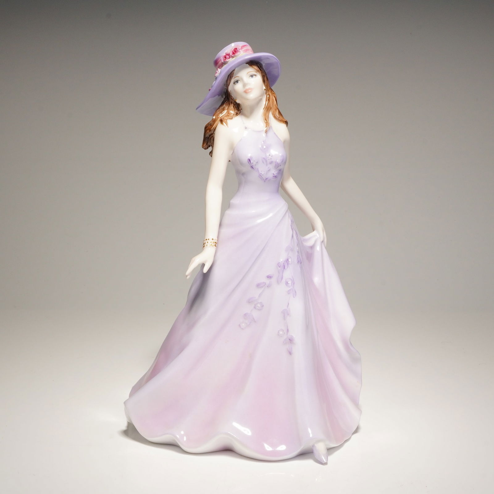 Coalport Ladies of Fashion Collection Figurine, Emma: A Coalport Emma from the Ladies of Fashion collection, modeled by Jack Glynn. The hand-decorated porcelain figure depicts a woman with auburn hair wearing a lilac and lavender halter-neck gown with fl