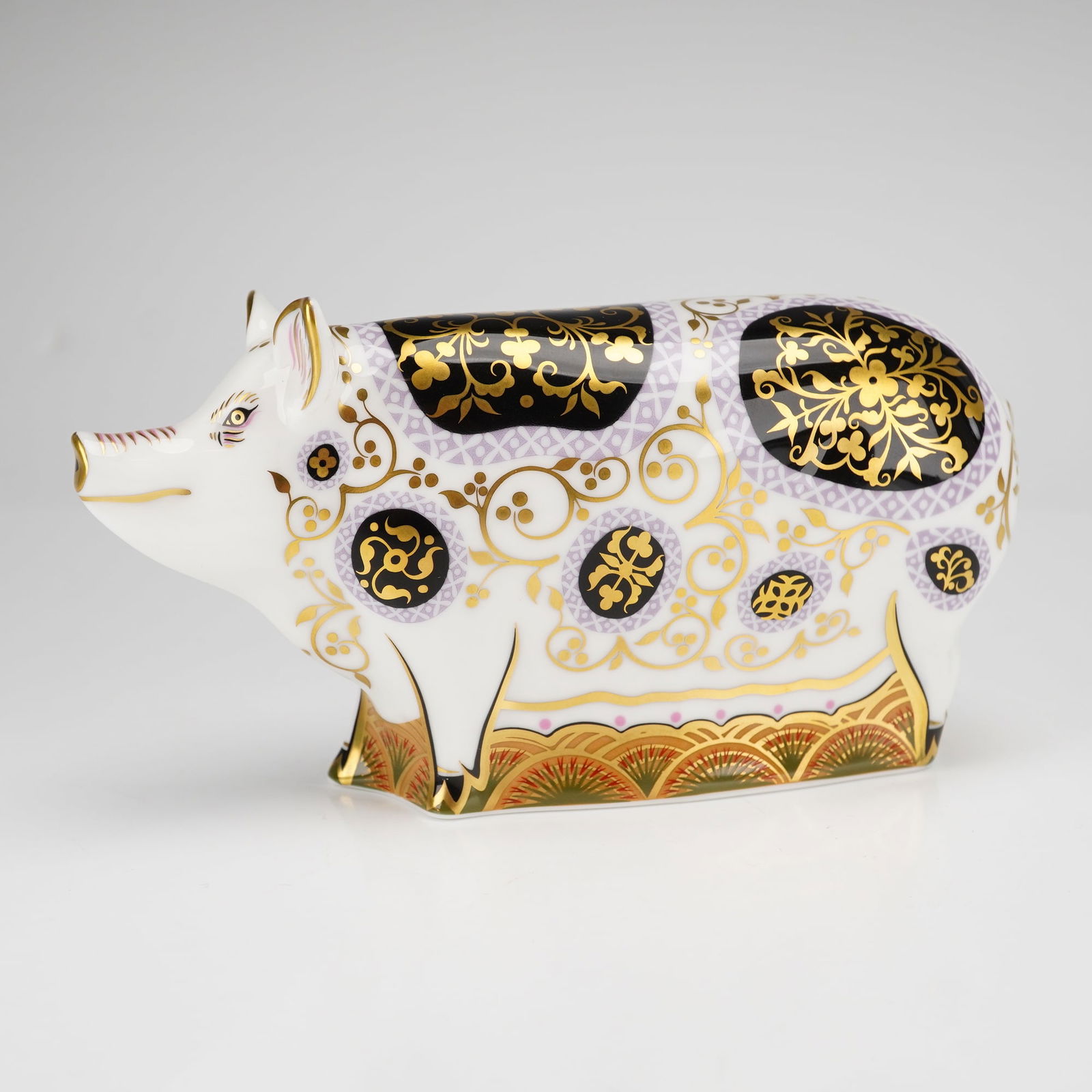 Royal Crown Derby Paperweight, Spotty Pig: This stylized figurine features intricate floral and scrolling patterns in gilt and navy blue, accented with purple-patterned circular motifs on a white ground. The base is finished with a tiered fan