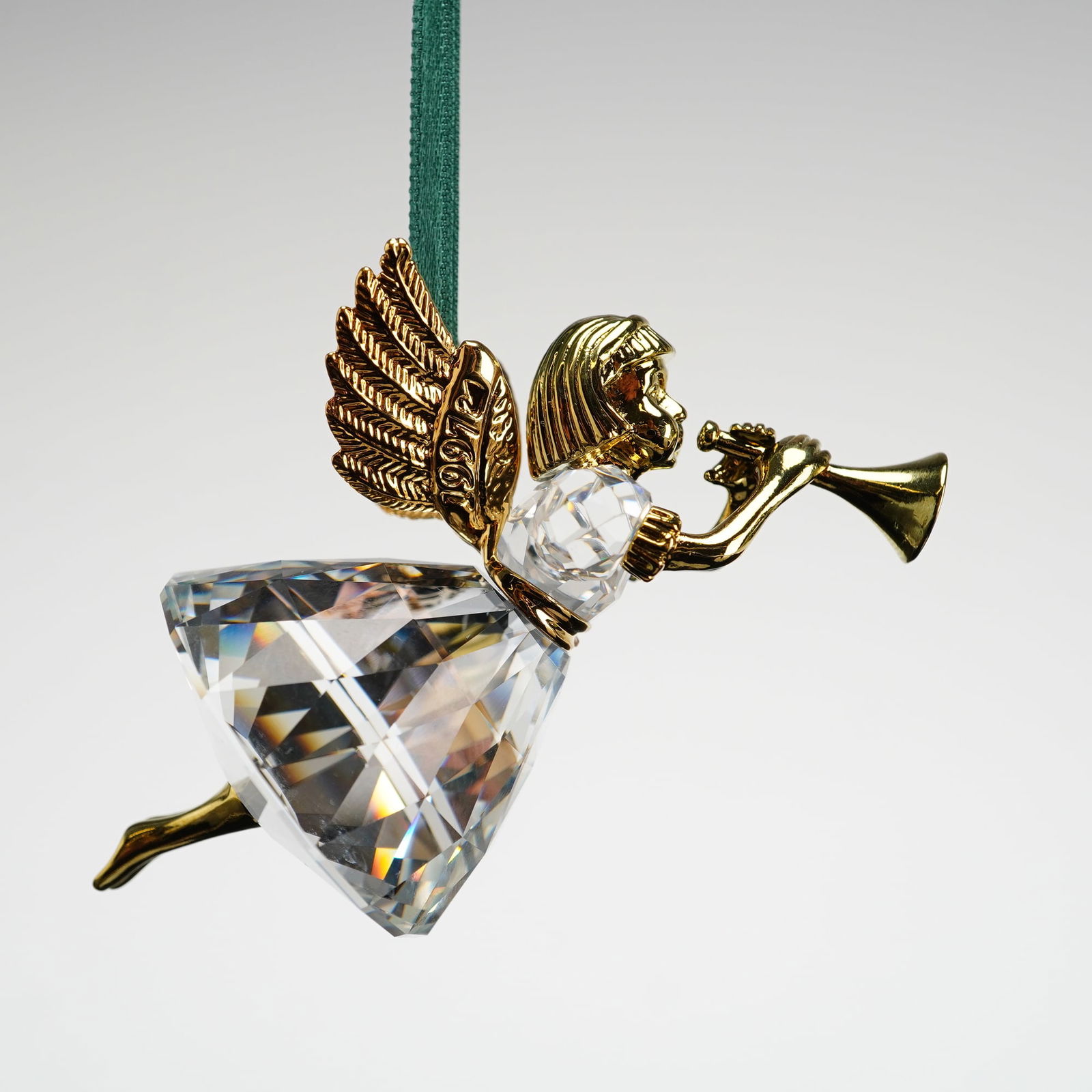 Swarovski Crystal Christmas Memories 1997 Angel Ornament: Ornament is depicting a flying angel playing a trumpet. The piece is constructed with a faceted clear crystal skirt and bodice, joined with polished gold-toned metal wings, head, arms, and instrument.