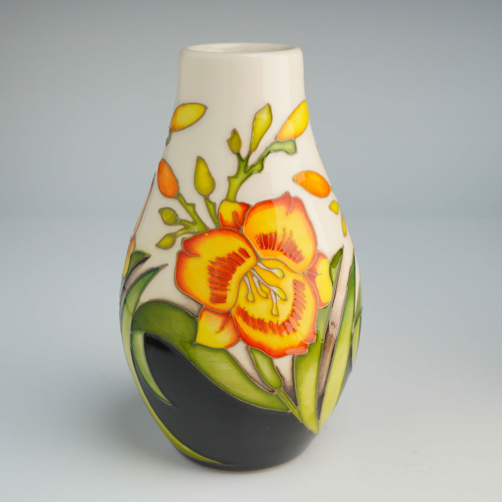 Moorcroft Pottery by Nicola Slaney Vase, Fooled Me: This ceramic vessel of ovoid form features tube-lined decoration depicting yellow and orange daylilies with green foliage. The floral motif is set against a contrasting cream and black ground. The und
