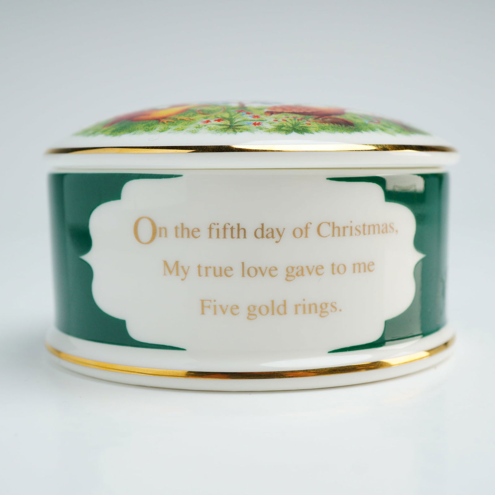 Wedgwood Bone China Lidded Box, Five Gold Rings: A Wedgwood round bone china lidded box, part of the Twelve Days of Christmas series, commemorating Five Gold Rings. The circular box features a dark green exterior band with a white cartouche inscribe
